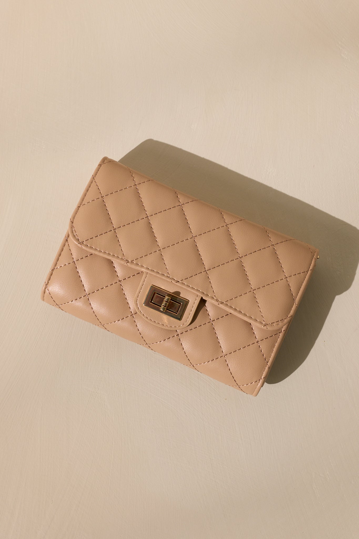 Overhead view of a beige quilted clutch bag with a front turn-lock closure.