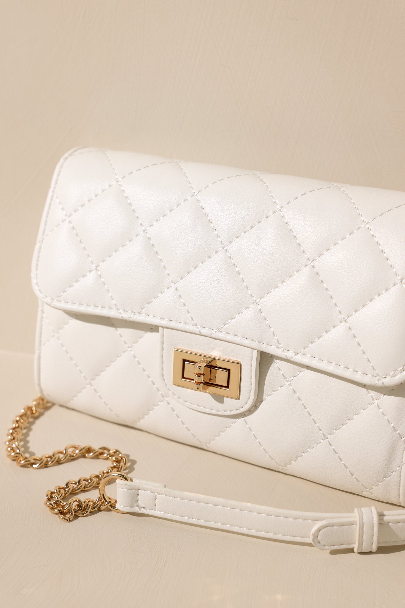 Stand alone view of this white bag that features gold hardware, a quilted design, turn lock closure, a zipper pocket inside, and a detachable chain shoulder strap.
