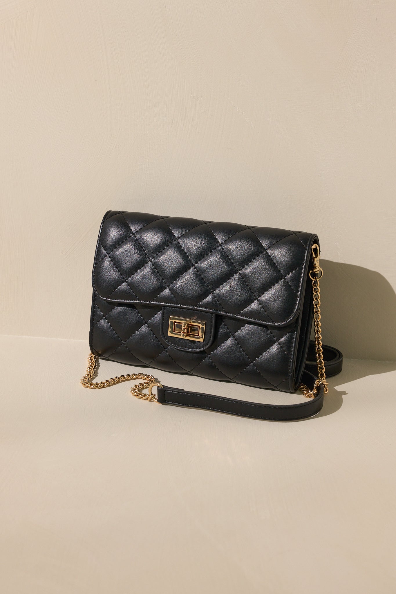 Stand alone view of this black bag that features gold hardware, a quilted design, turn lock closure, a zipper pocket inside, and a detachable chain shoulder strap.