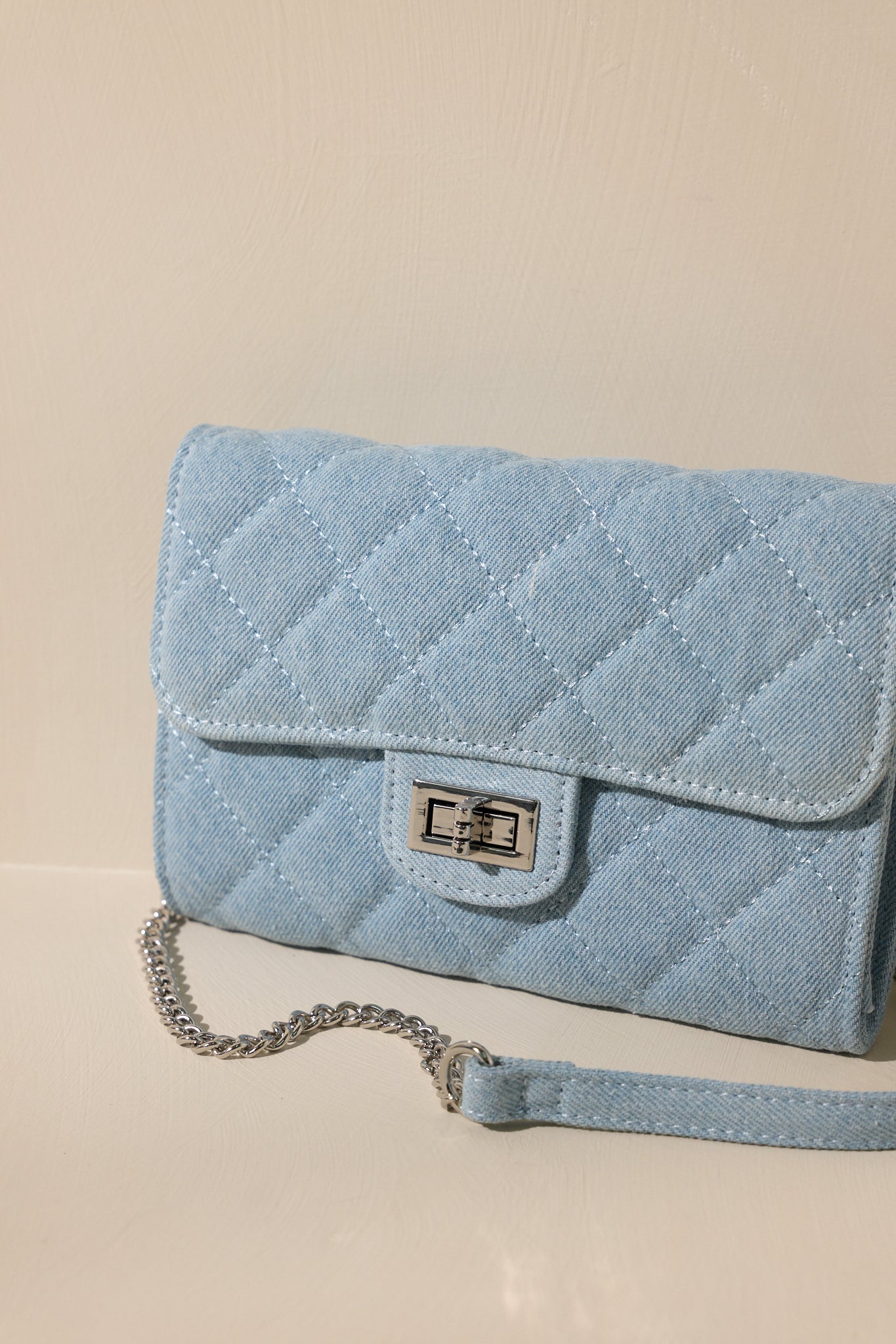 Close up view of this denim bag features silver hardware, a quilted design, turn lock closure, a zipper pocket inside, and a detachable chain shoulder strap.