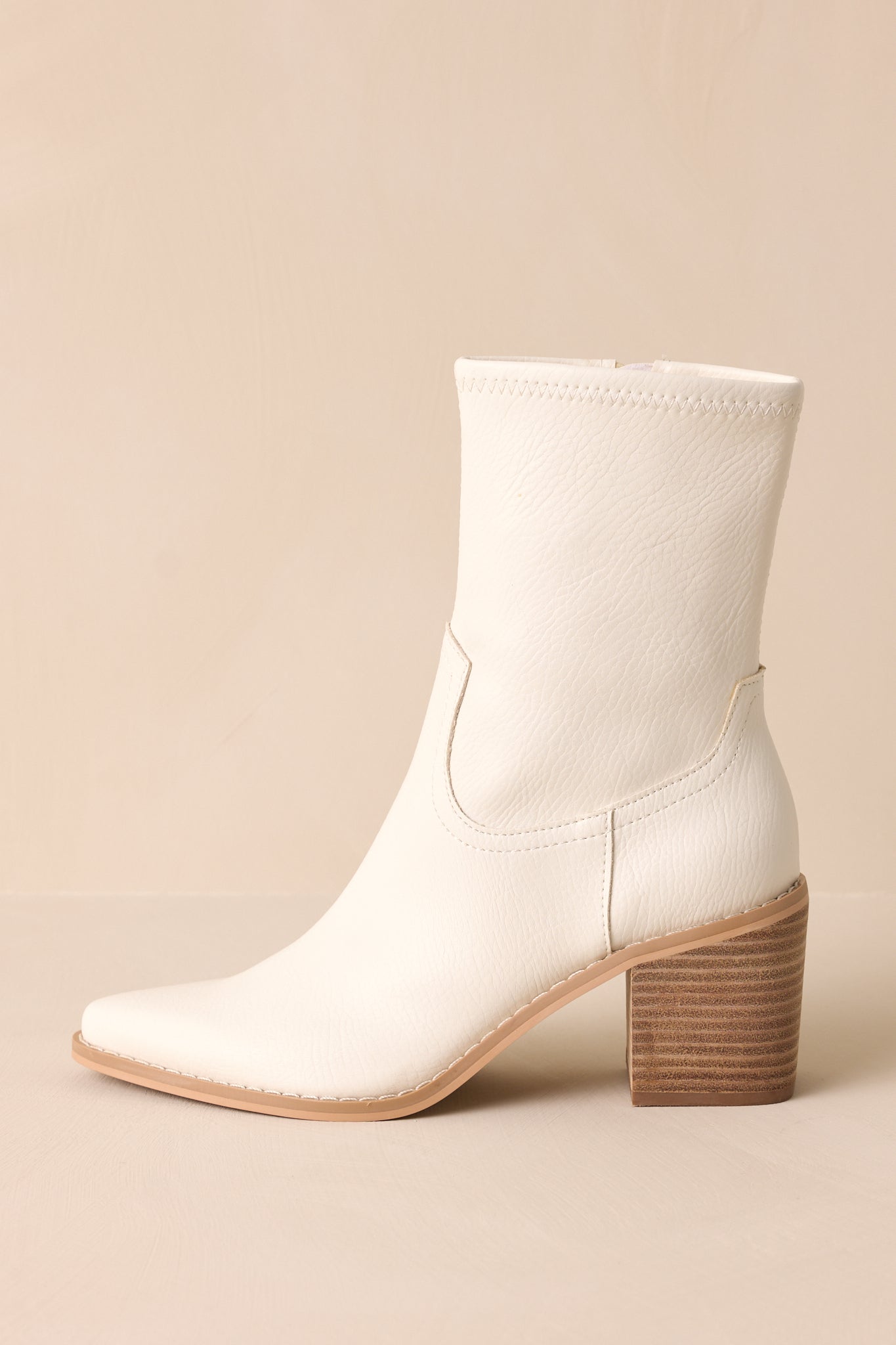 Close-up side view of these white boots that feature a pointed toe, a platform heel, a discrete side zipper and a tan sole.