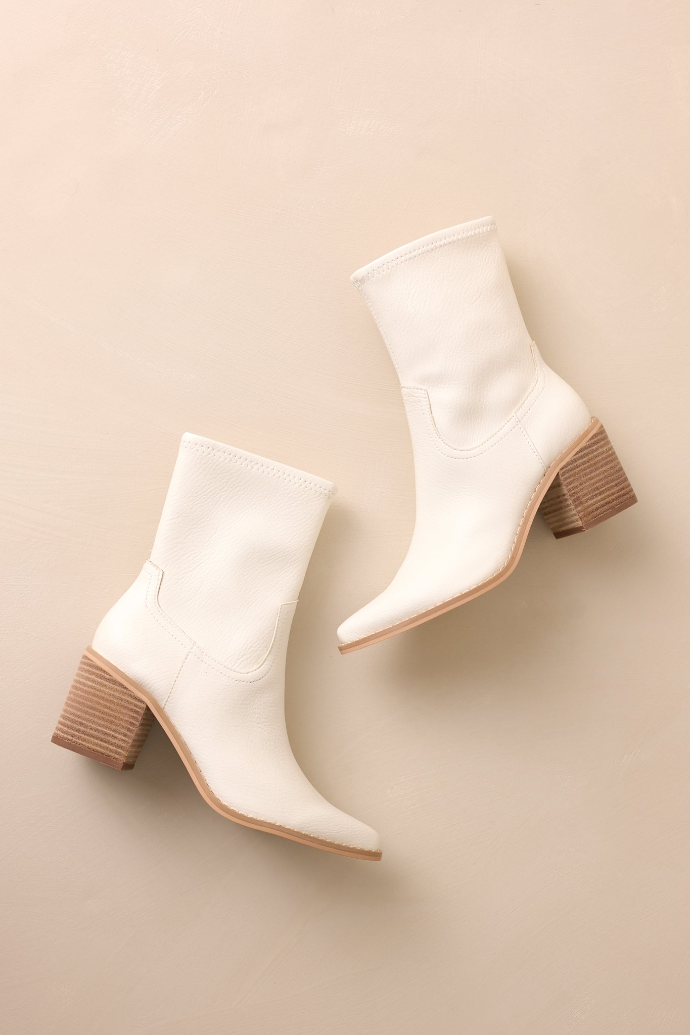 Overhead view of these white boots that feature a pointed toe, a platform heel, a discrete side zipper and a tan sole.