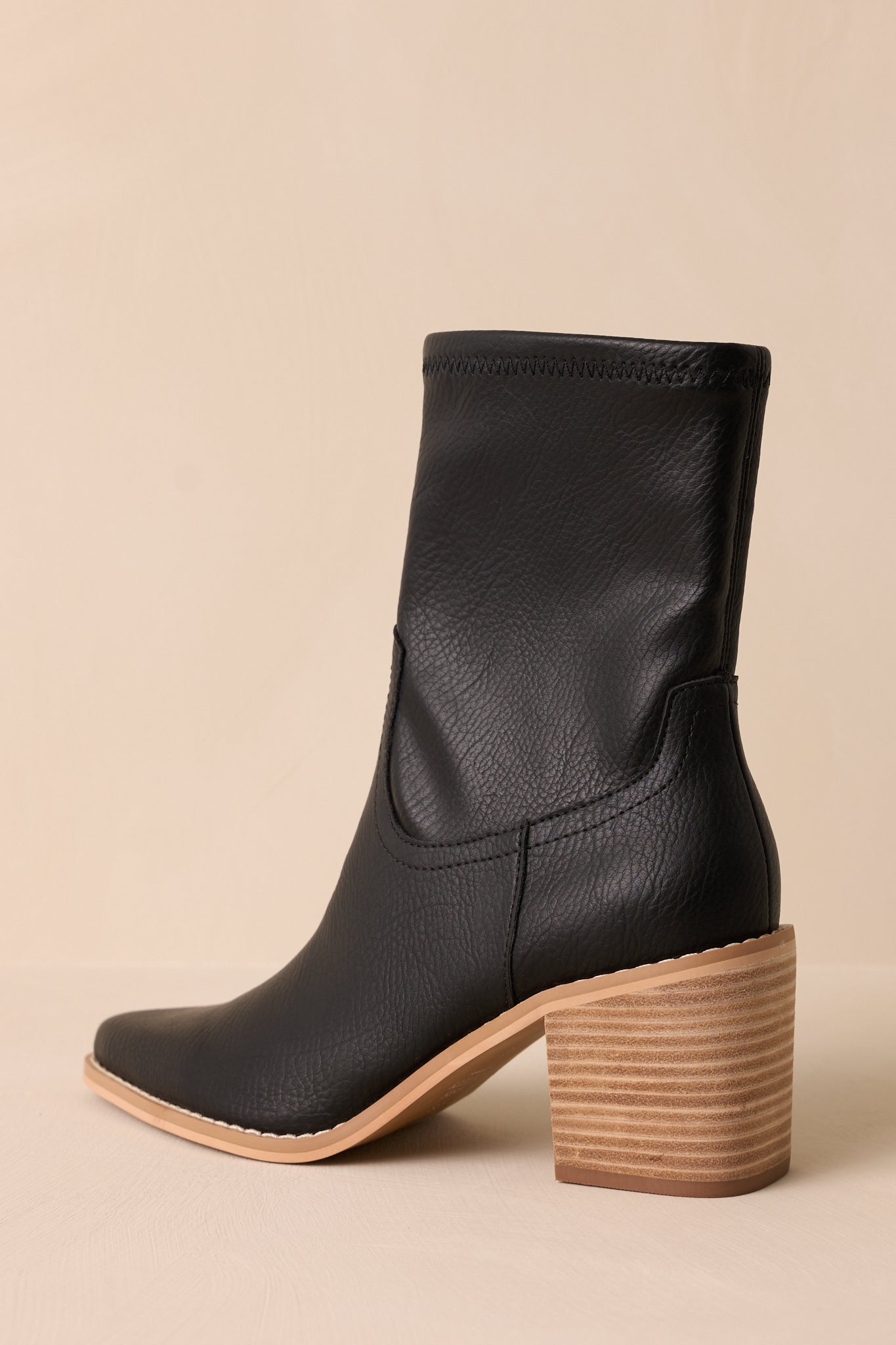 Back view of these black boots that feature a pointed toe, a platform heel, a discrete side zipper and a tan sole.