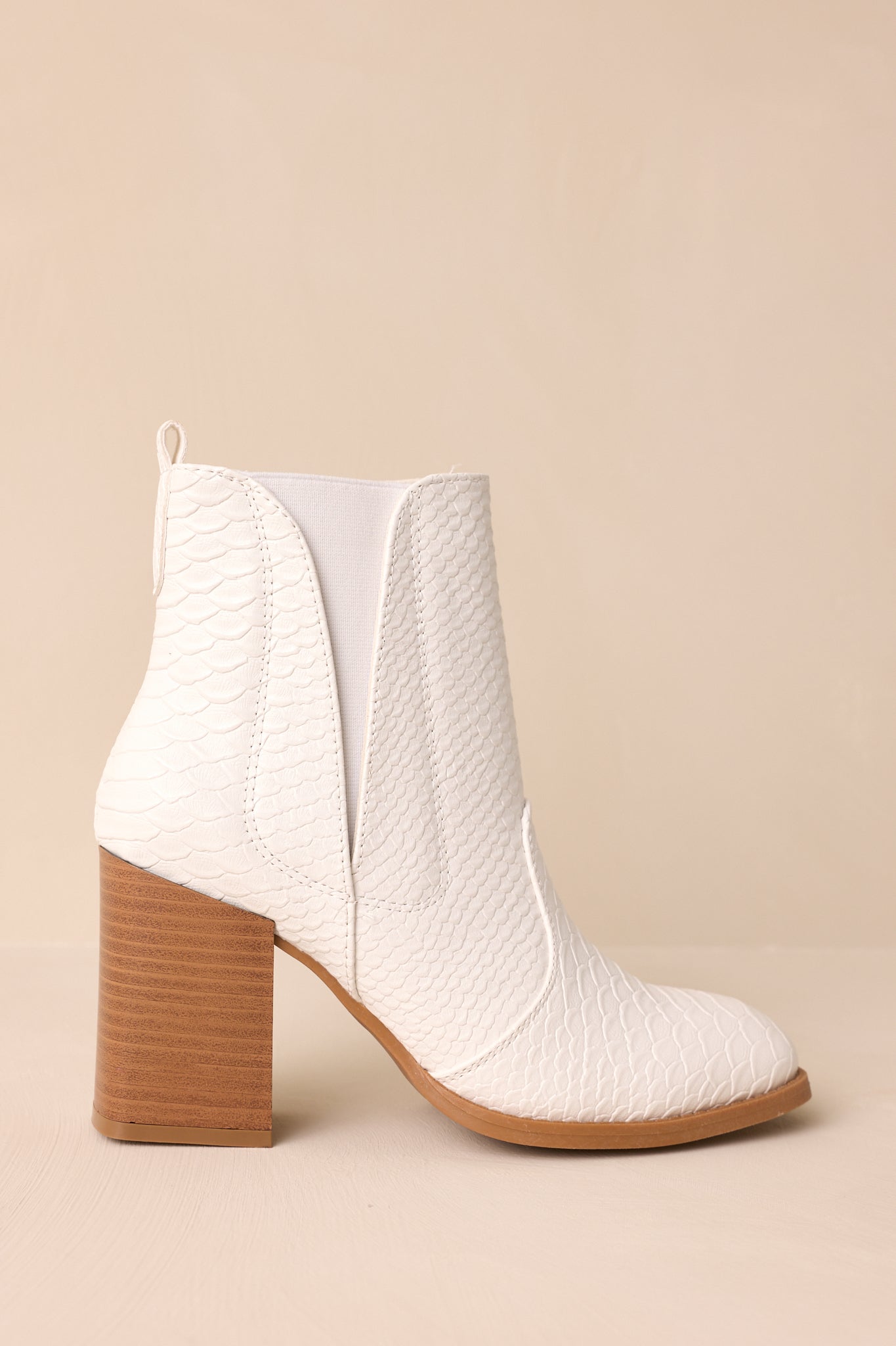 Angled side view of these white ankle boots that feature a square toe, a platform heel, a snake skin texture, a side zipper and an elastic side insert.