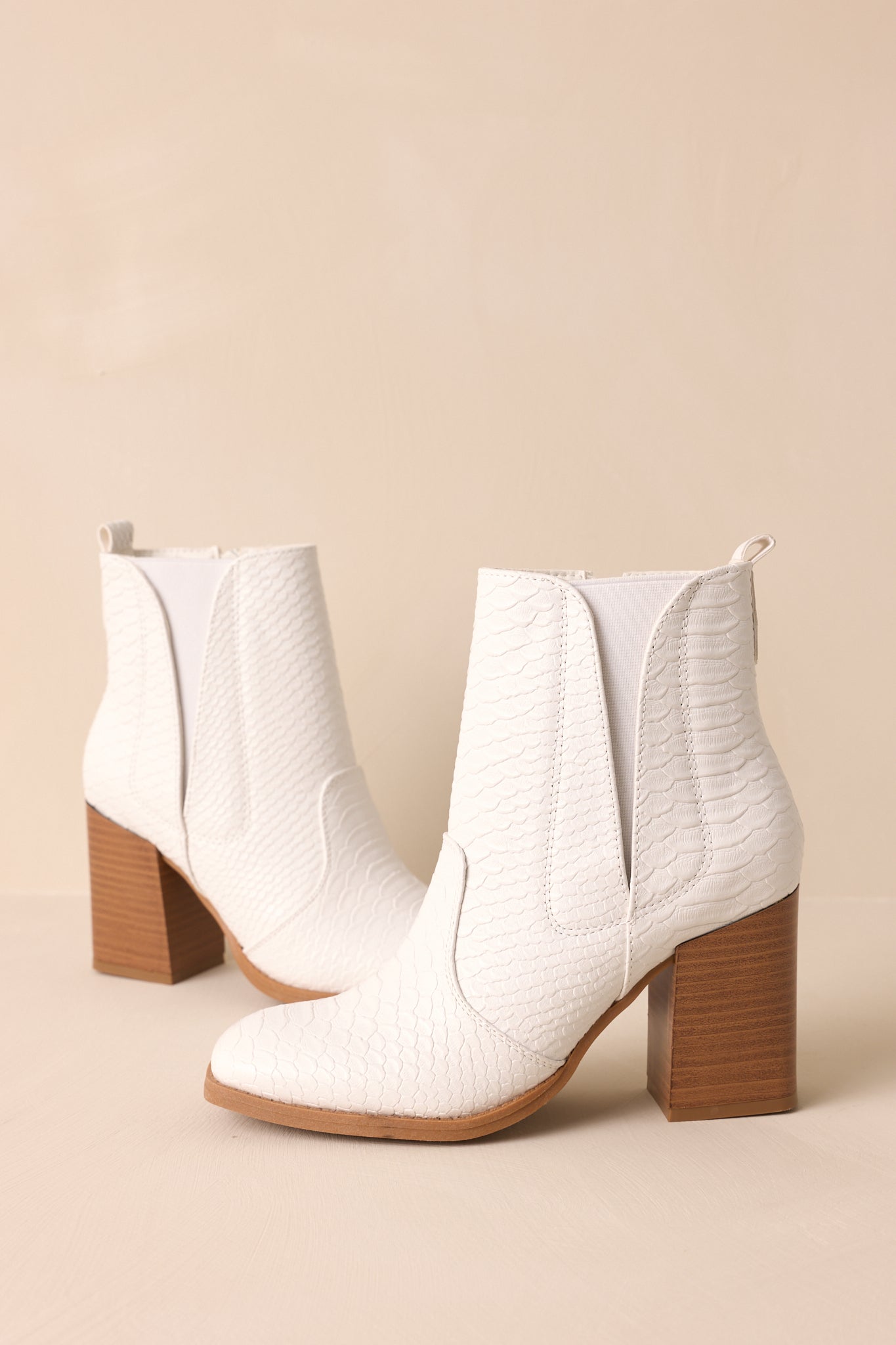 Side view of these white ankle boots that feature a square toe, a platform heel, a snake skin texture, a side zipper and an elastic side insert.
