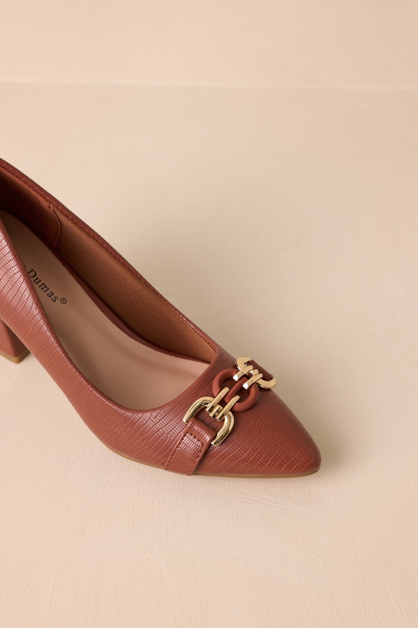 Close-up view of these brown heels that feature a crocodile pattern, block heel, gold hardware, and a pointed toe.