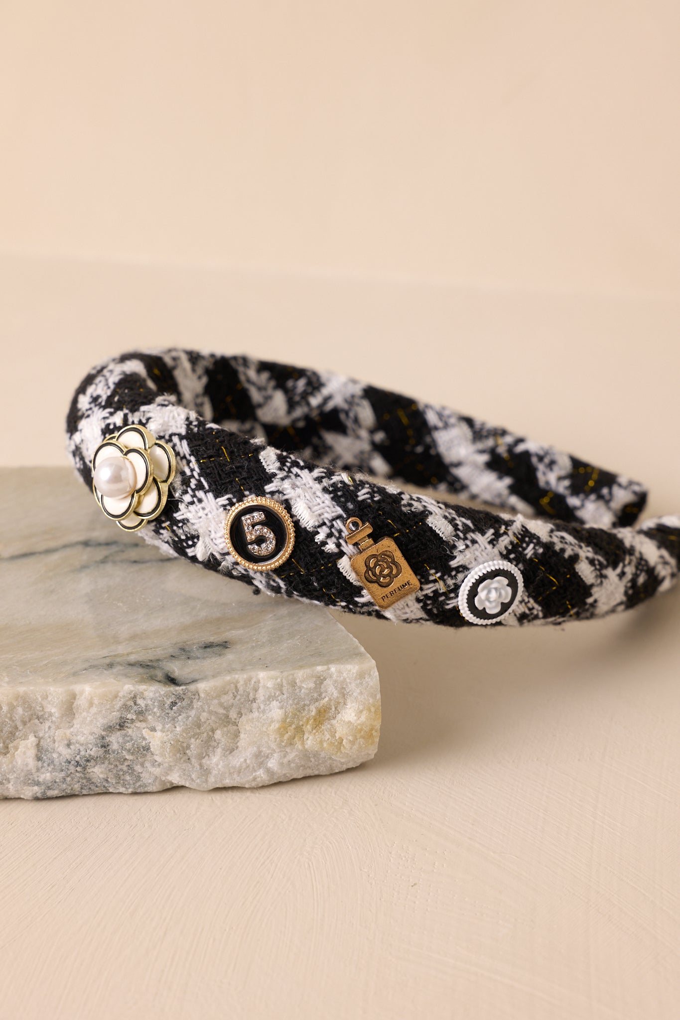 Angled close-up view of this headband that features a black and white tweed fabric, adorned with four adorable charms along one side.