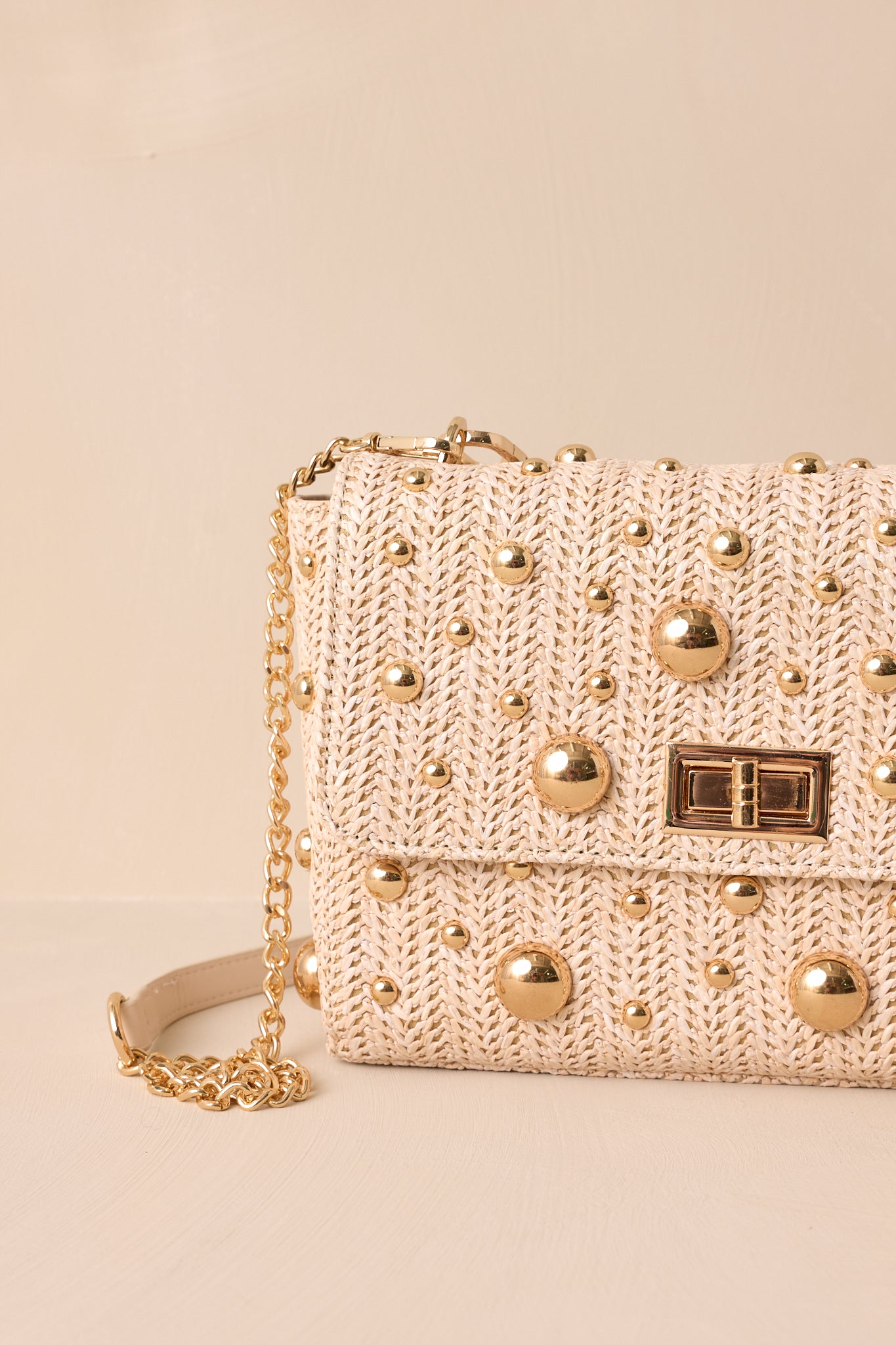 Close-up view of this rattan handbag that features a square shape, gold reflective polka dots, a gold turn closure, gold hooks for optional strap and a zippered pouch inside.