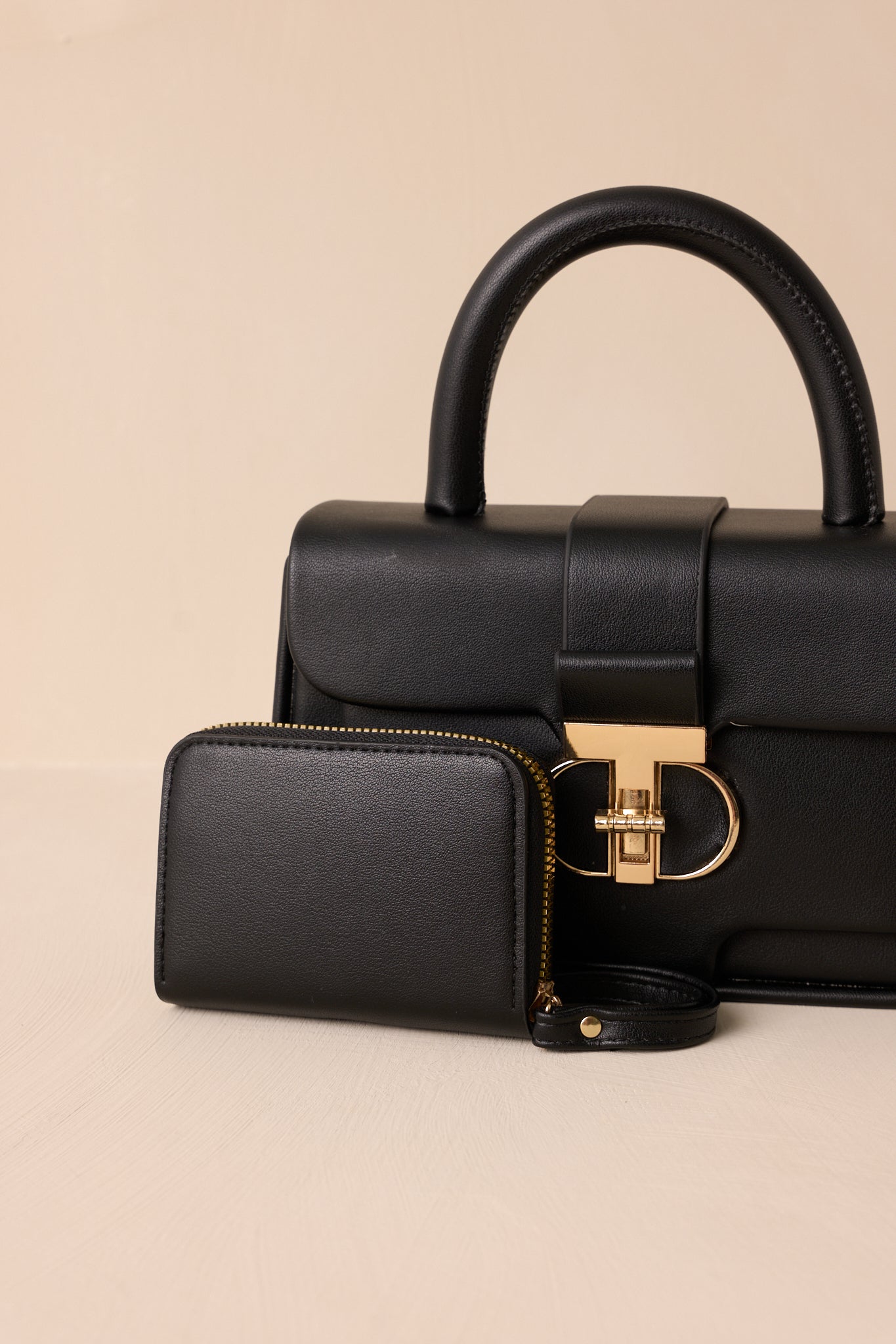 Close-up view of this black handbag that features a gold accent turn closure, a built in pocket, a matching mini wallet and gold accent side loops for exchangeable straps.