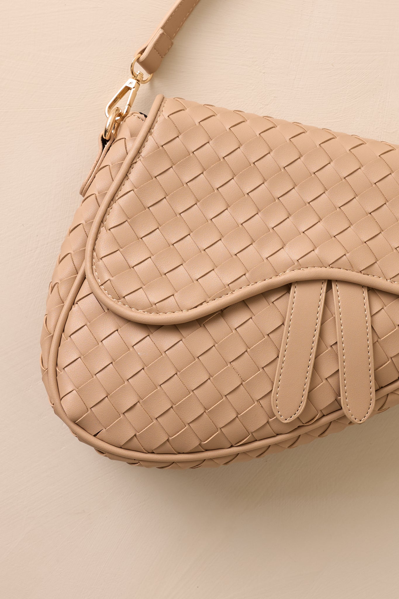 Close-up view of this beige handbag that features gold hardware, faux leather, a woven design, a magnetic snap closure, a zipper pocket, and an additional strap.