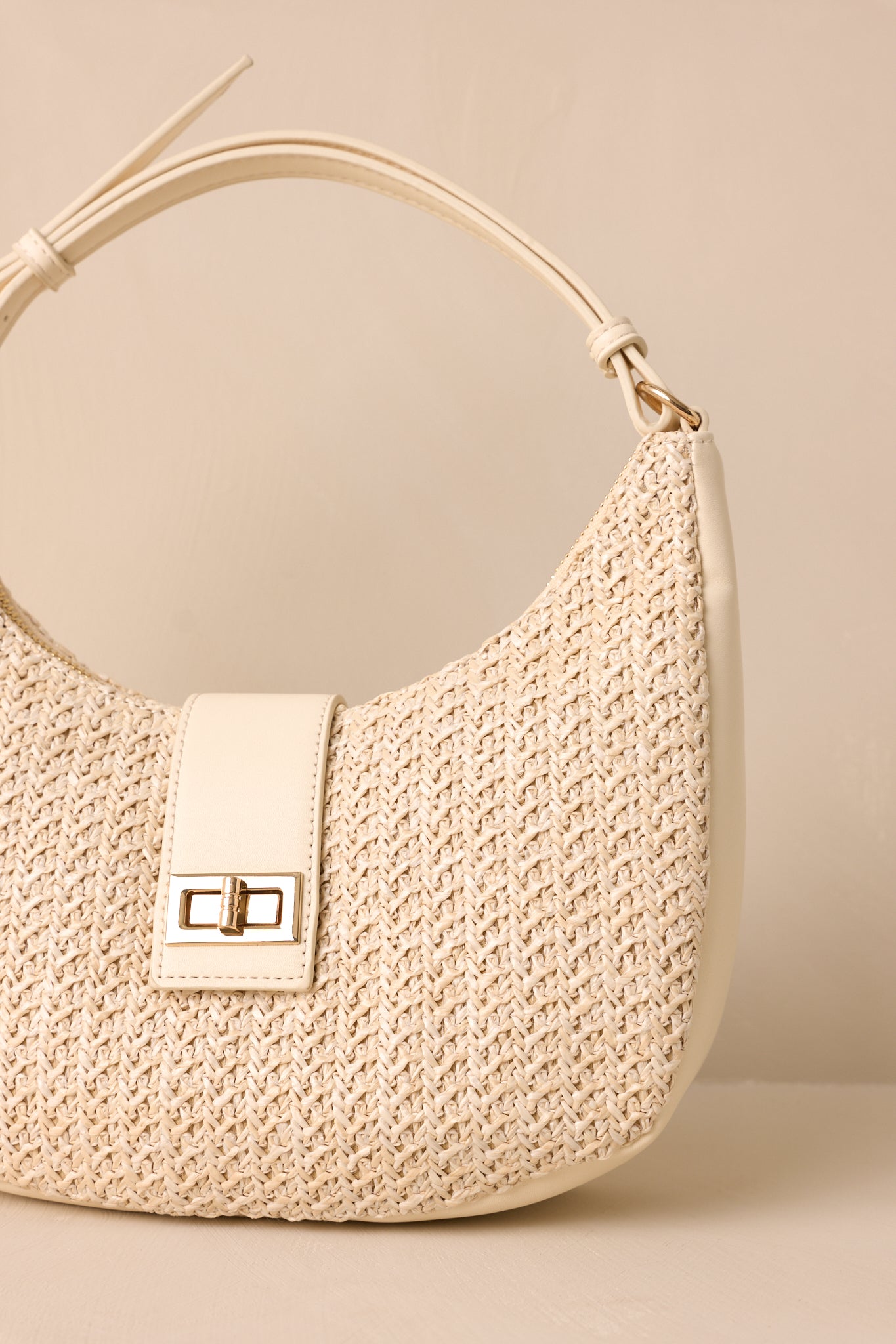 Close up of the woven texture, top flap strap closure, and turn lock fastening on this ivory handbag. 