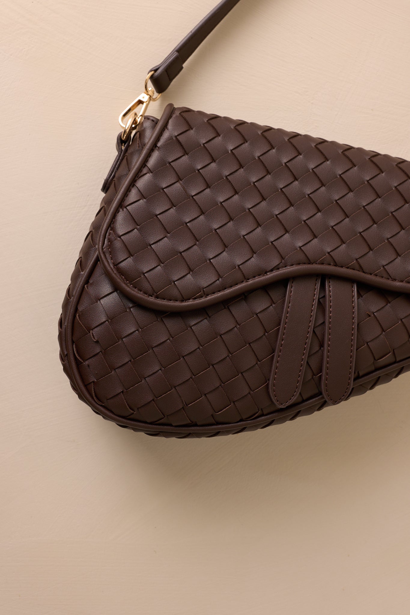 Close-up view of this brown handbag that features gold hardware, faux leather, a woven design, a magnetic snap closure, a zipper pocket, and an additional strap.