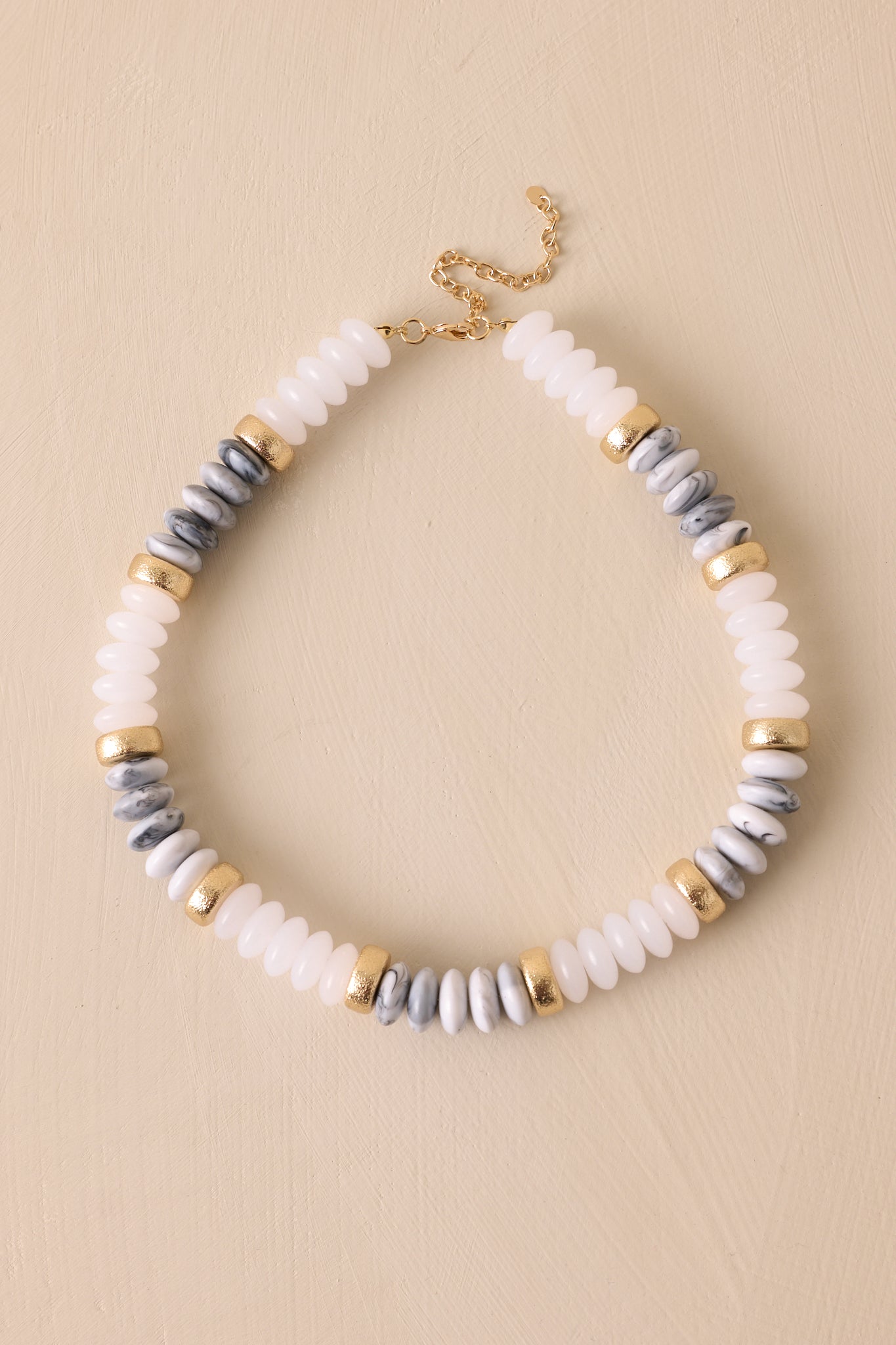 This ivory necklace features gold hardware, ivory, gold, and marbled flat beads, and a lobster clasp closure.