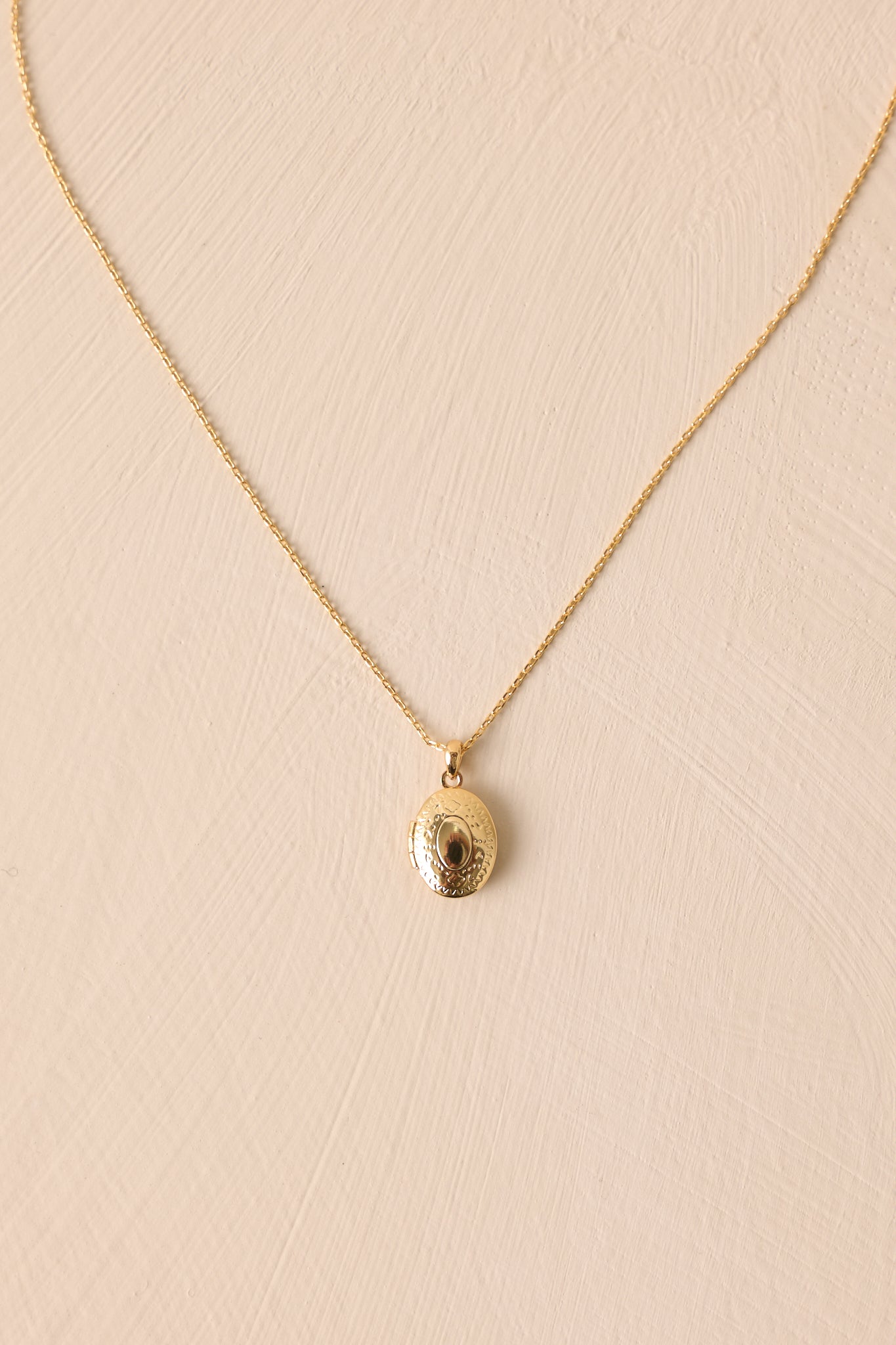 Over-head view of this gold locket that features gold hardware, an oval locket, and an adjustable length.