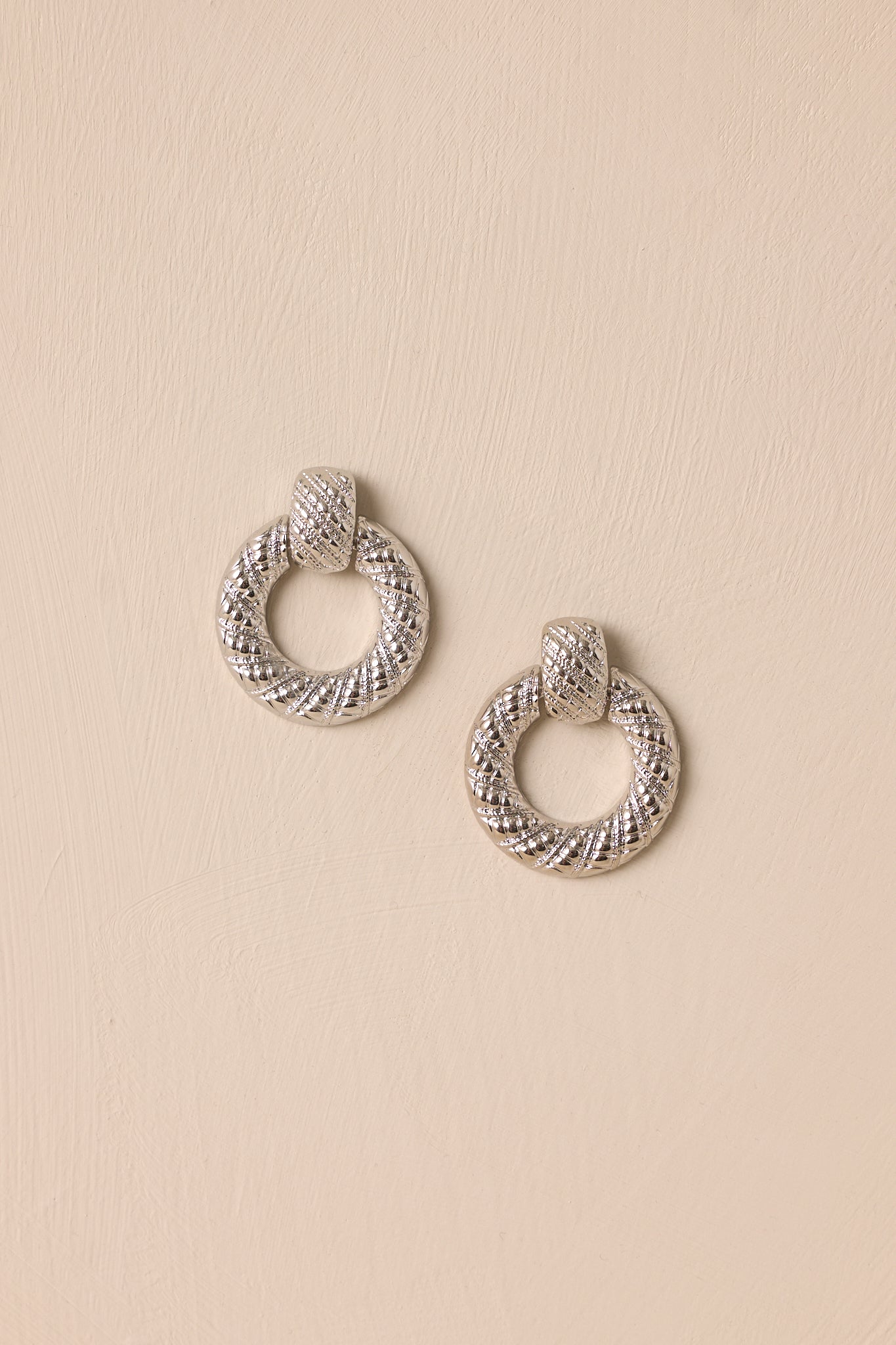 Overhead view of these silver earrings that features a ridged stud with a connected hoop with the ridges increasing in size.