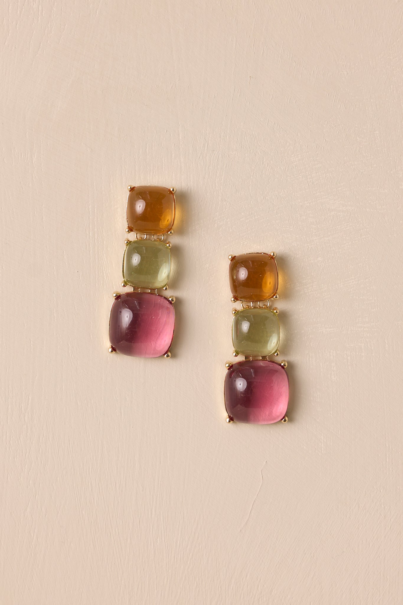 Flat view of earrings featuring gold hardware, an orange stone stud, green and pink drop stones, and a secure post backing.