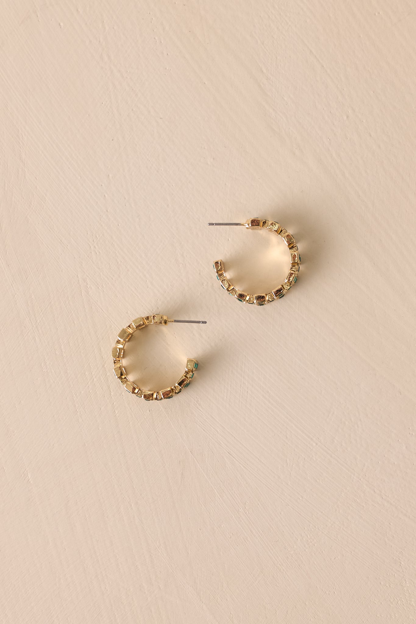 A pair of gold incomplete hoop earrings with a checkered pattern of green rhinestones along the band. The earrings are shown lying flat on a neutral background with secure back postings visible.