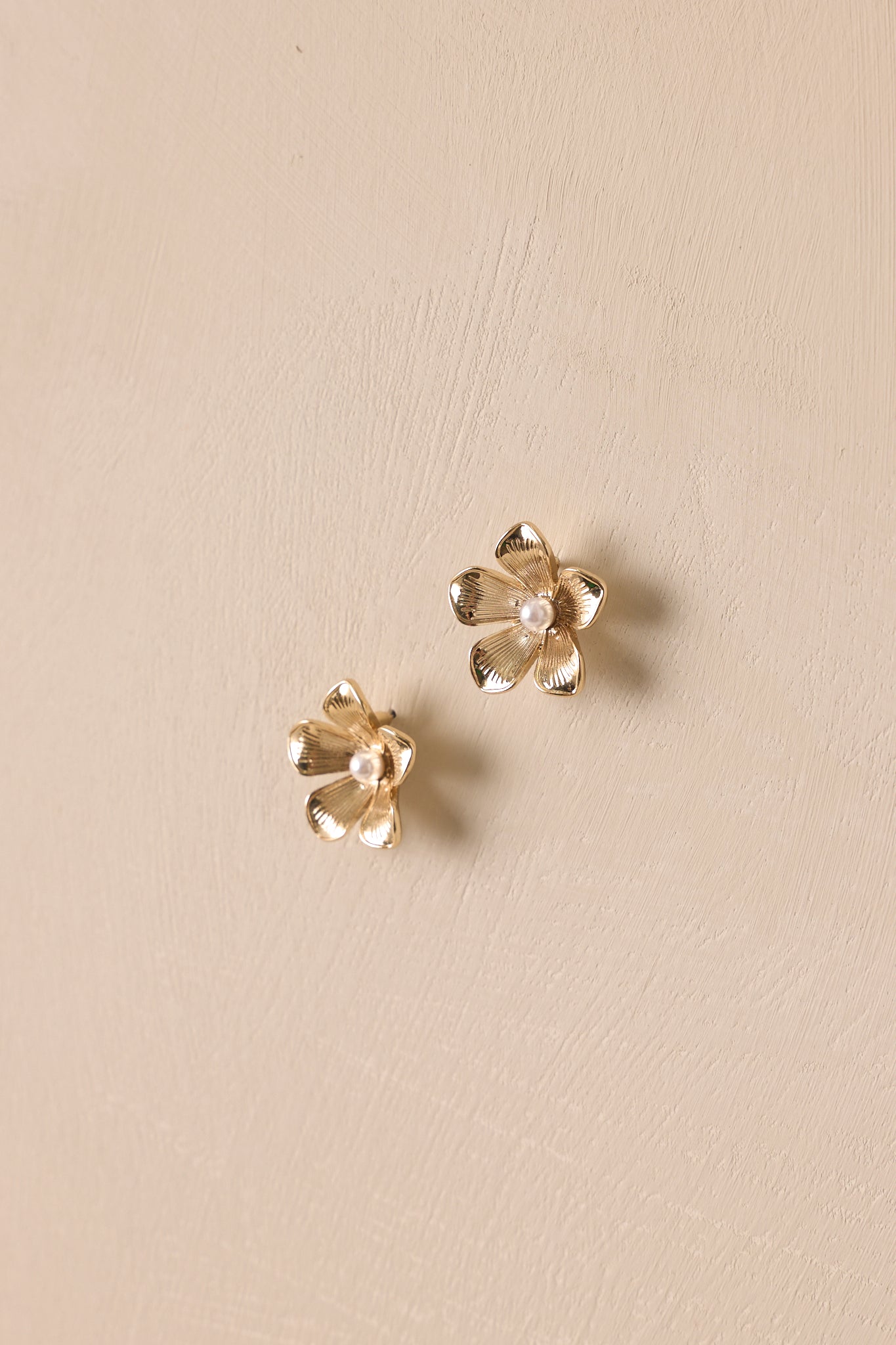 Angled view of these gold earrings that feature a floral shape, a pearl center, and secure post backings.