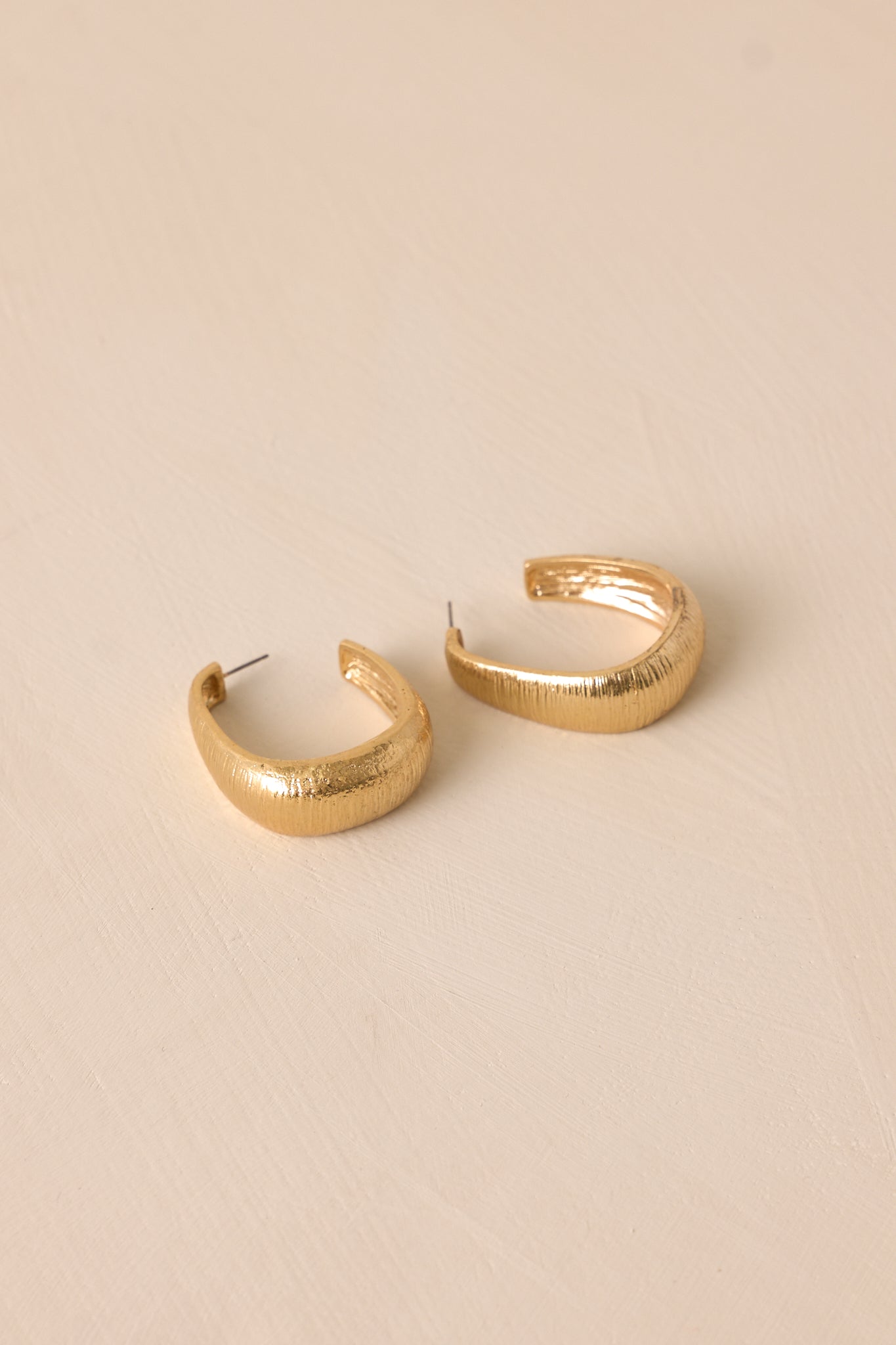 Angled view of these earrings that feature a square hoop shape, a gold textured design and a secure post backing.