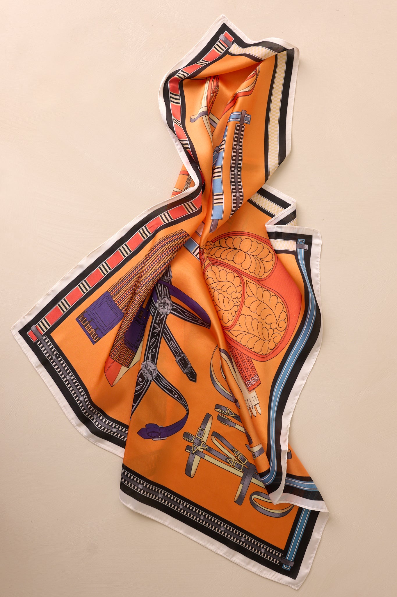 Front view of an orange multi print scarf featuring a satin material, a black and white trim and a multi color design.