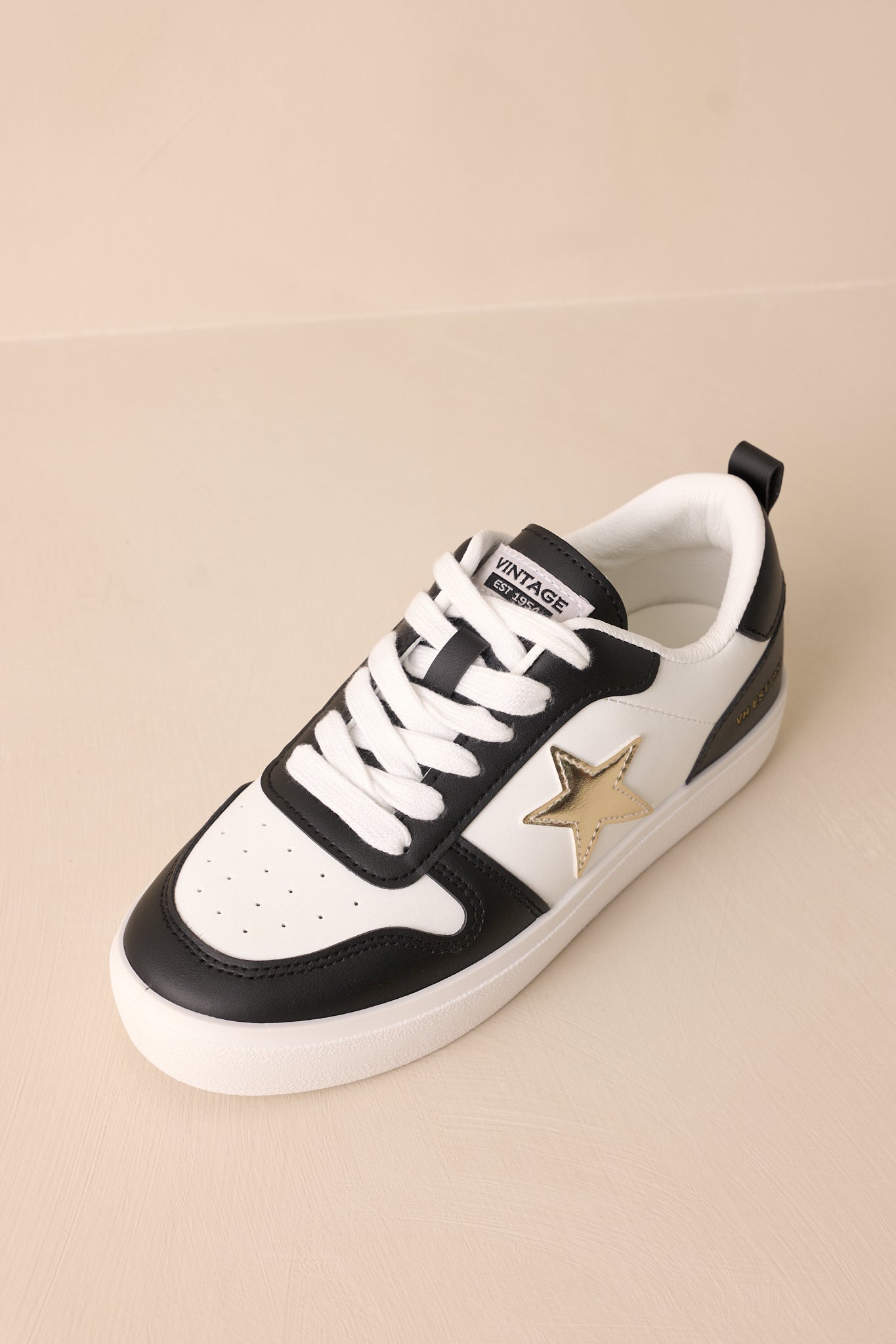 Overhead view of these black sneakers that feature a rounded toe, functional white laces, interchangeable gold laces, a comfortable fit, a gold star detailing, and a thick sole.