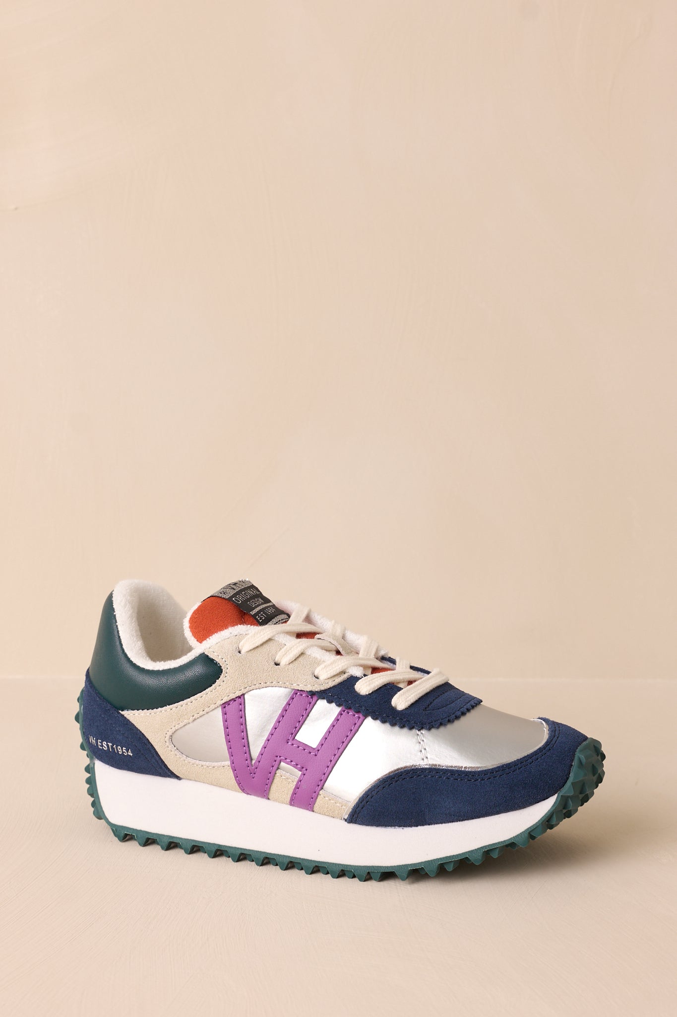 Angled front view of these silver sneakers that feature a rounded toe, functional laces, subtle pops of purple, navy, orange and silver, a slight platform, and a heavily textured sole.