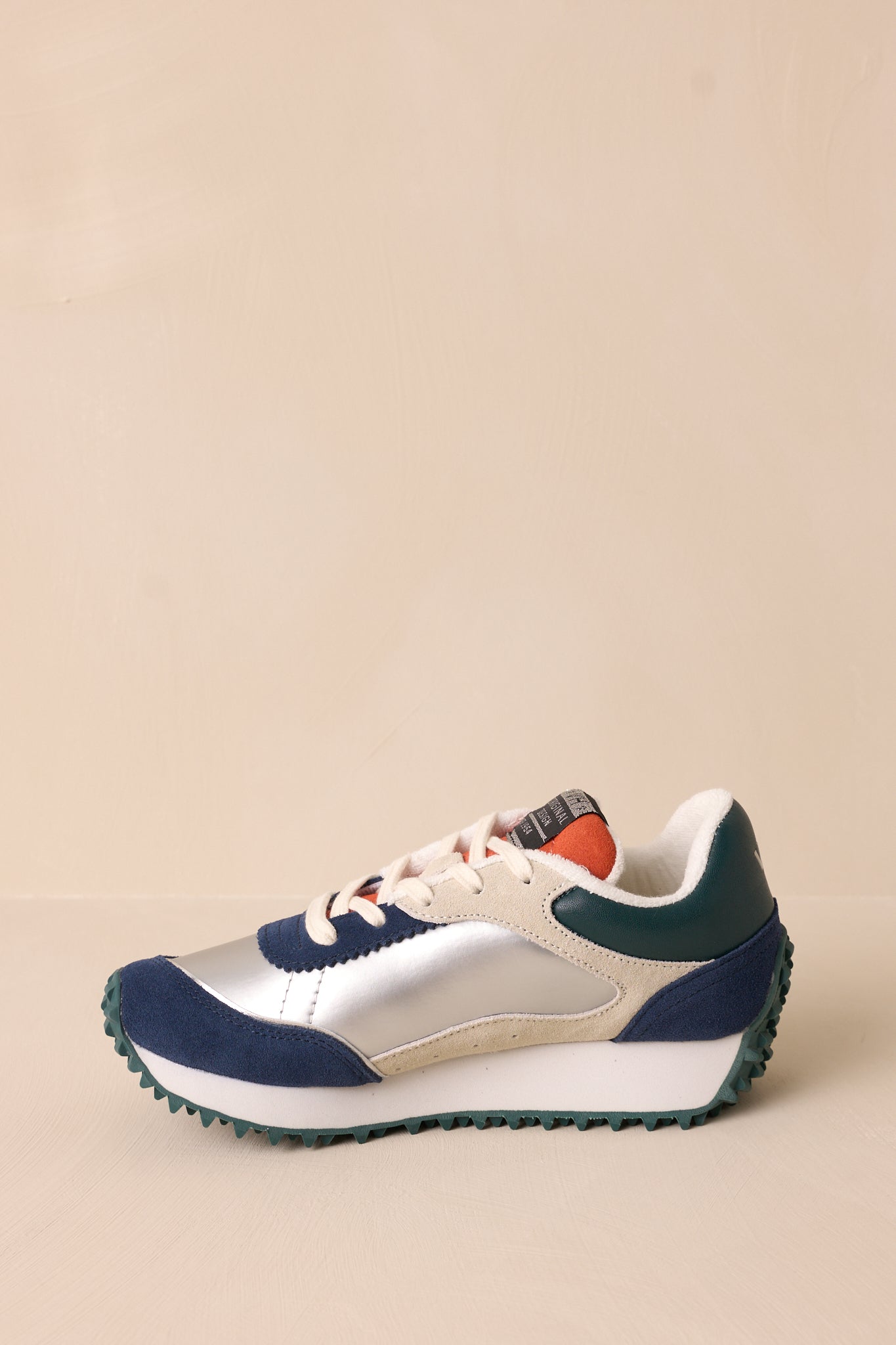 Inside side view of these silver sneakers that feature a rounded toe, functional laces, subtle pops of purple, navy, orange and silver, a slight platform, and a heavily textured sole.