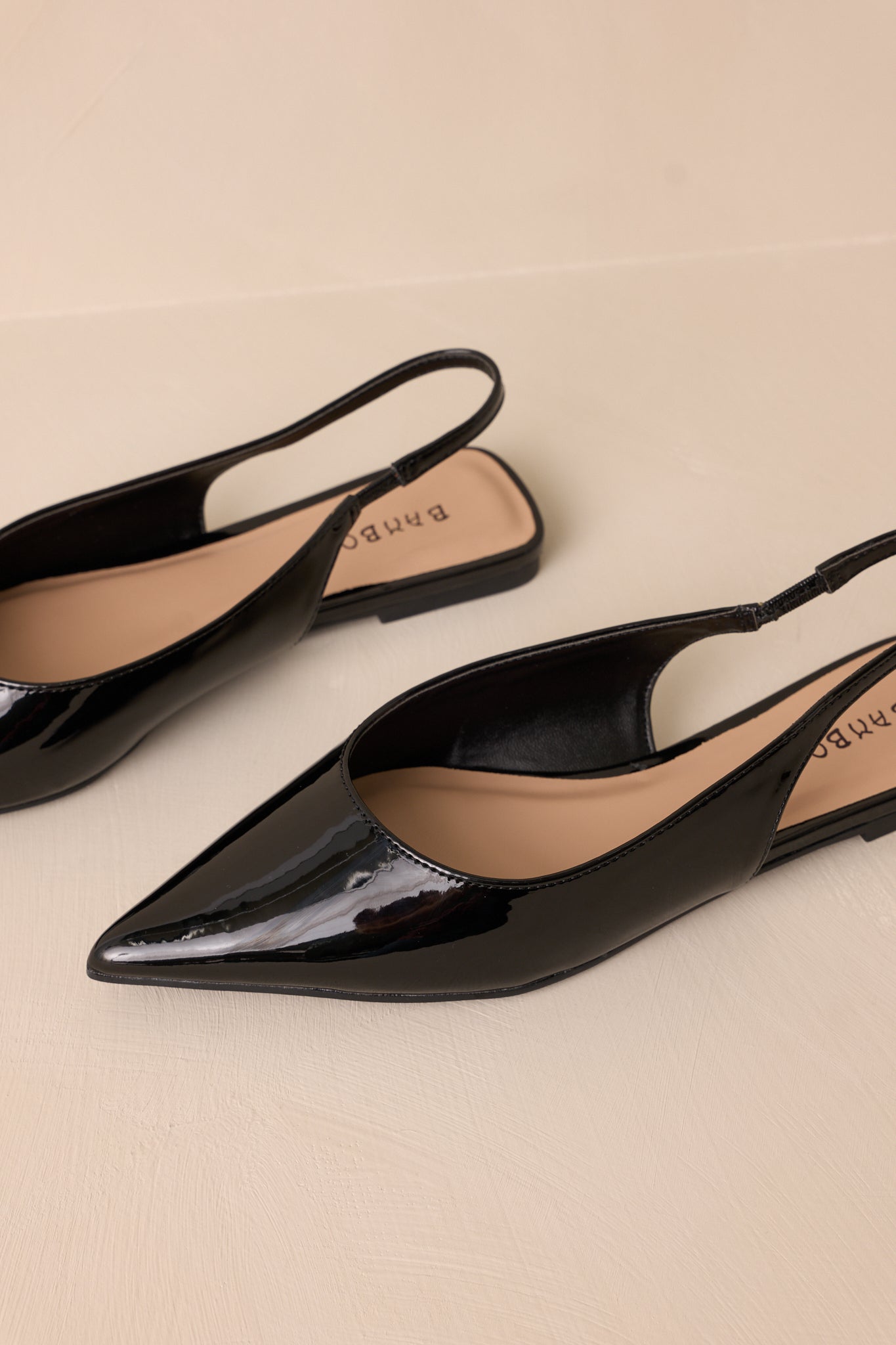 These black flats feature a pointed toe, a faux leather texture, a slingback-style strap, and a sleek black color.