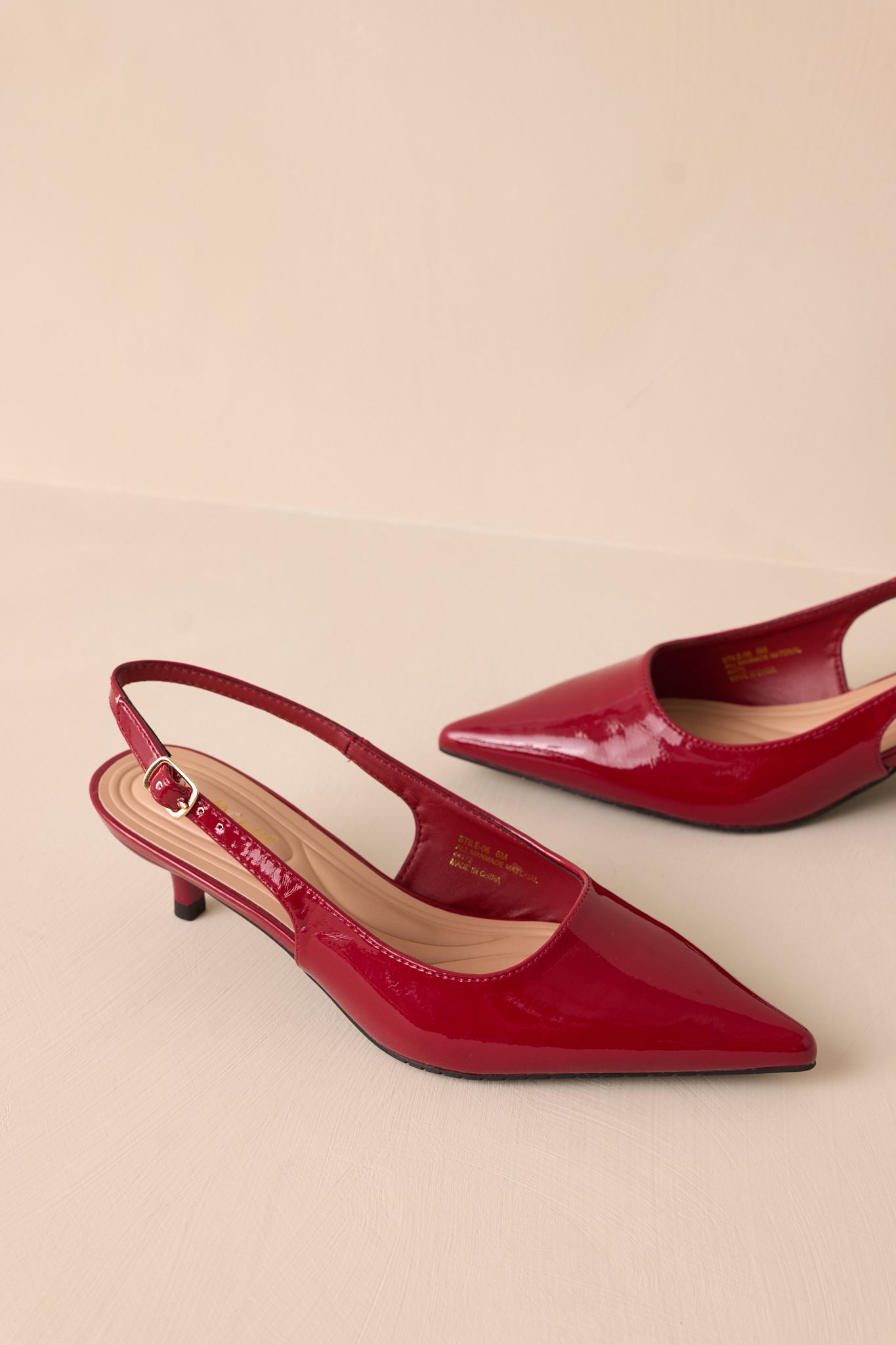 Side angle of a single burgundy heel with a pointed toe, glossy patent material, and adjustable slingback strap, highlighting the short kitten heel and cushioned insole for comfort.