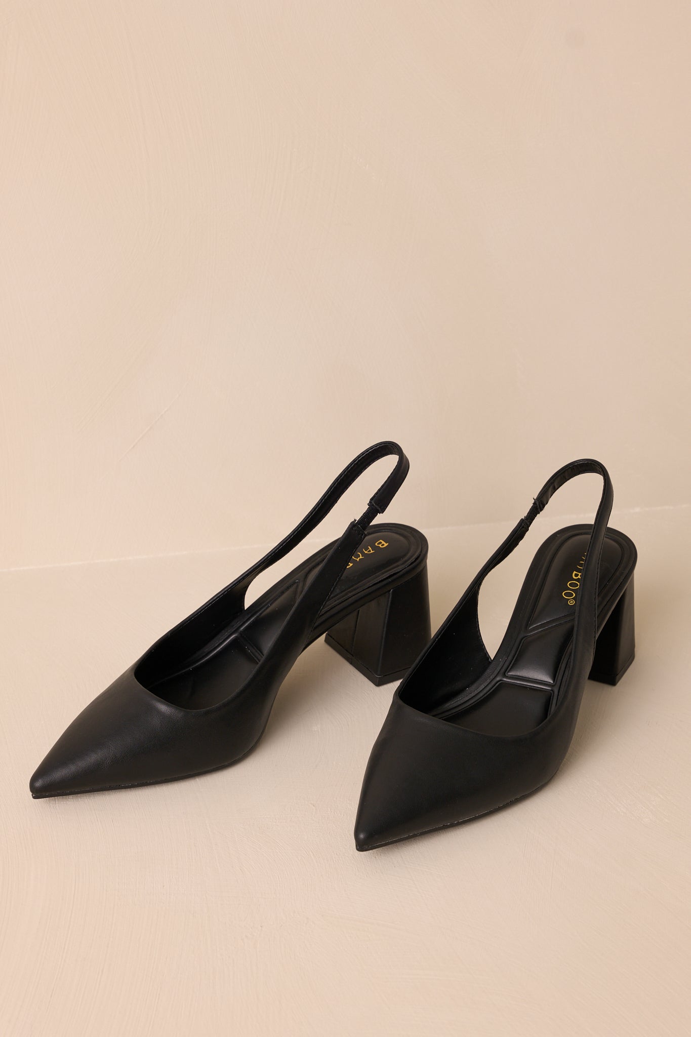 Detailed view of black heels with a strap around the back of the foot, showcasing the elegant pointed toe and sturdy block heel.