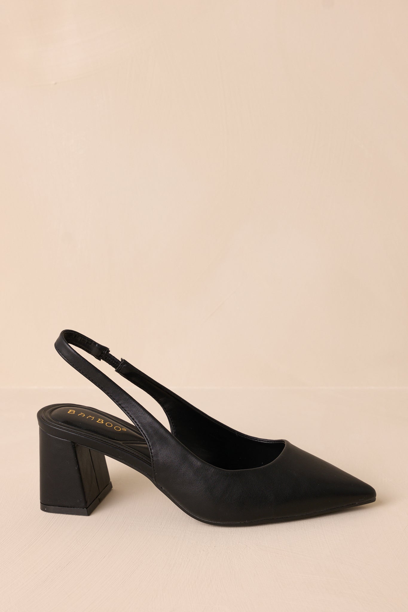 Detailed view of black heels with a strap around the back of the foot, showcasing the elegant pointed toe and sturdy block heel.