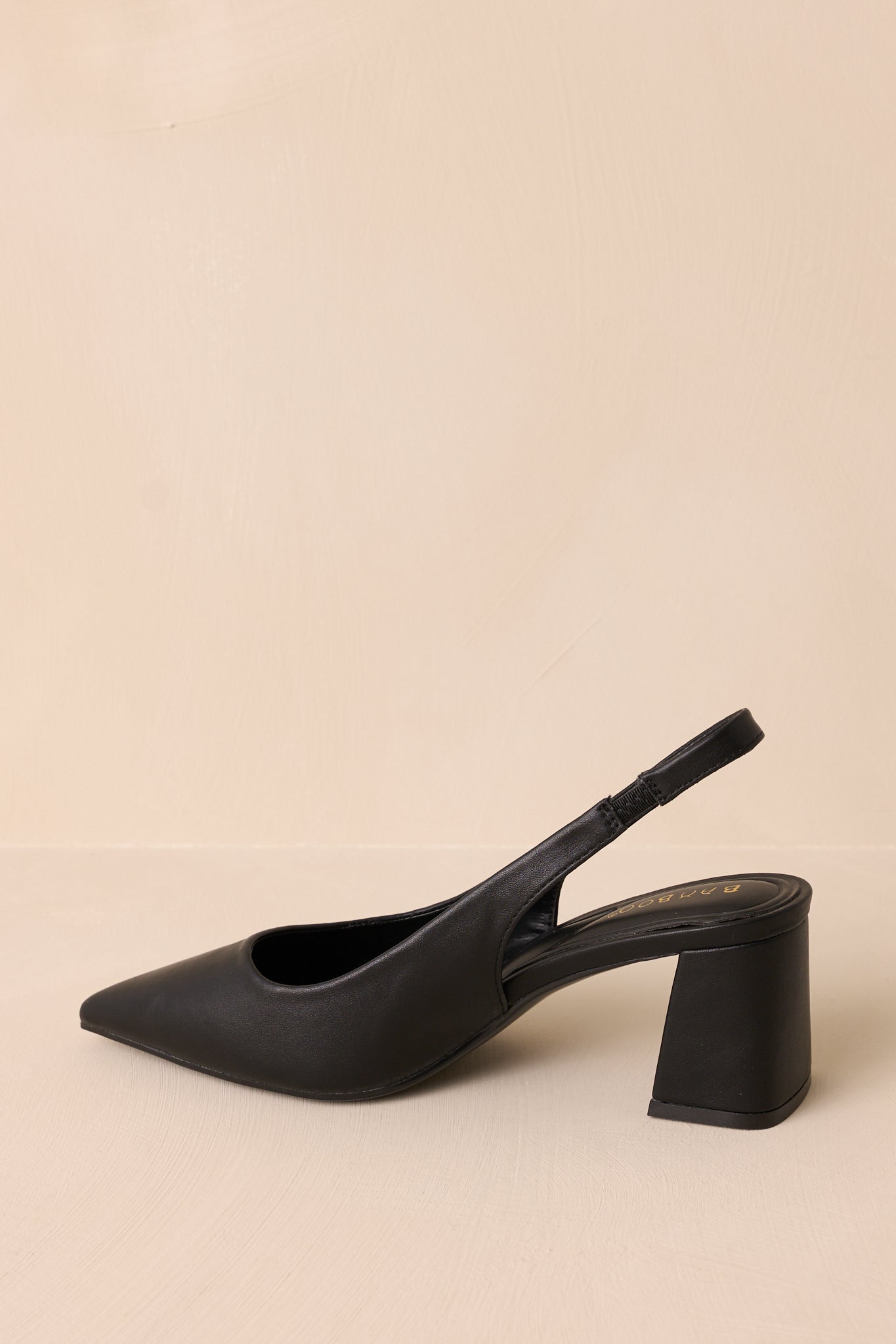 Front view of the black heels, showcasing the pointed toe and the shine of the faux leather material.