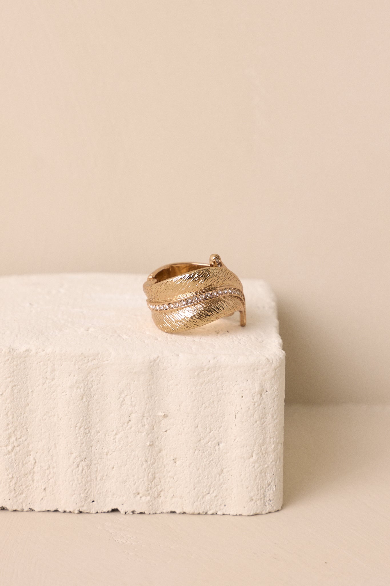 Side view of a gold ring featuring textured gold hardware, a split band, a feathered design, a line of rhinestones through the middle of the ring to the tips of the feathers.