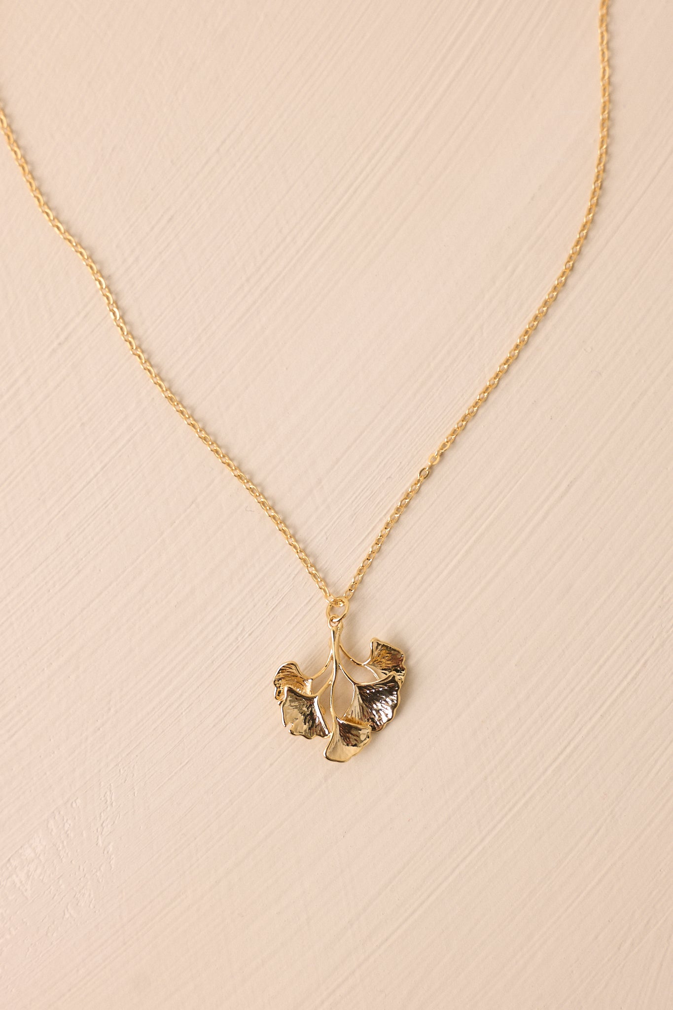 A close-up of the gold wildflower pendant on the necklace, highlighting the fine details of the pendant and the thin gold chain.