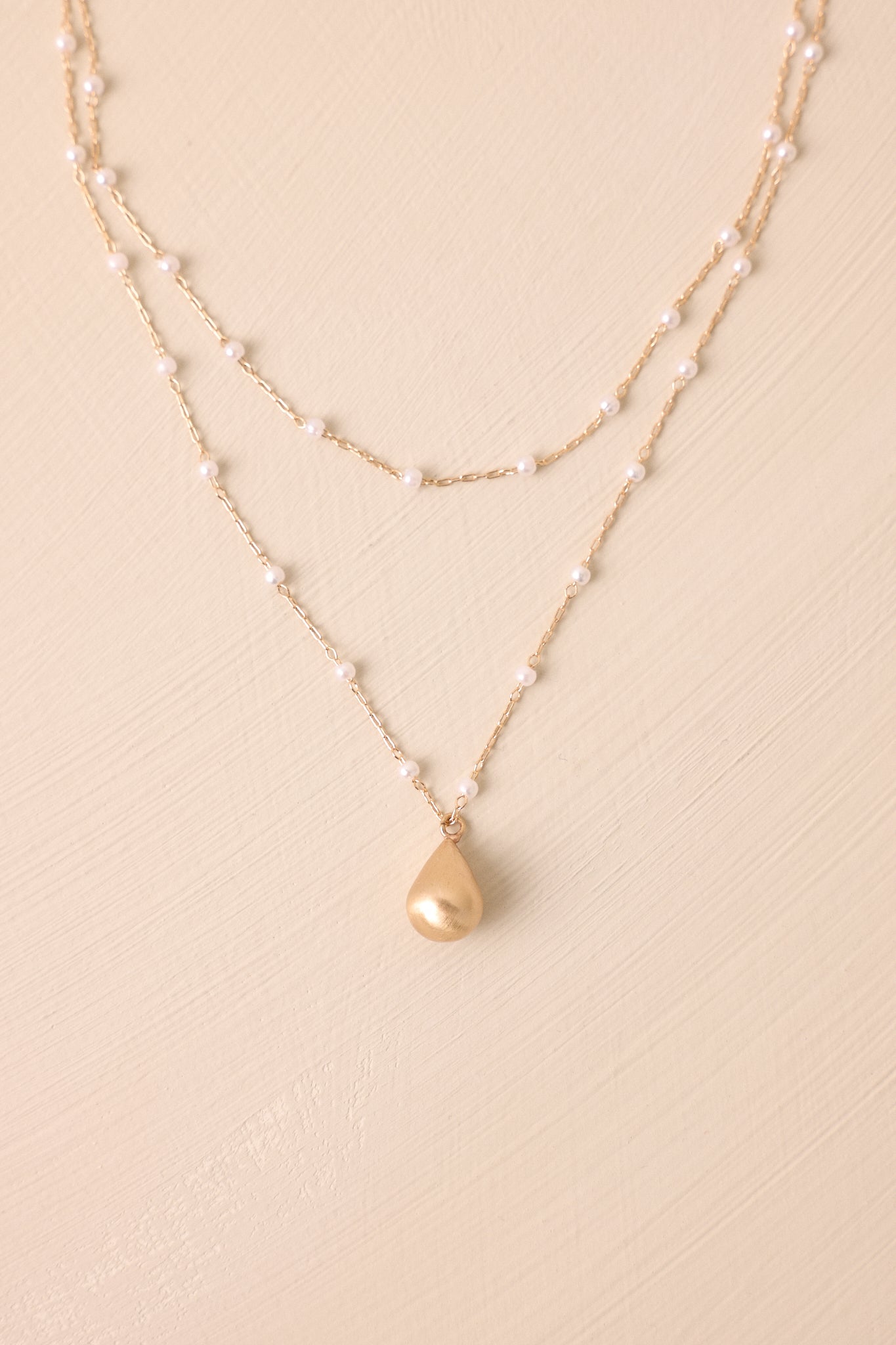 A detailed close-up of the necklace focusing on the craftsmanship of the gold hardware, highlighting the texture of the chains, the gleam of the teardrop pendant, and the lustrous faux ivory pearls nestled among the links.