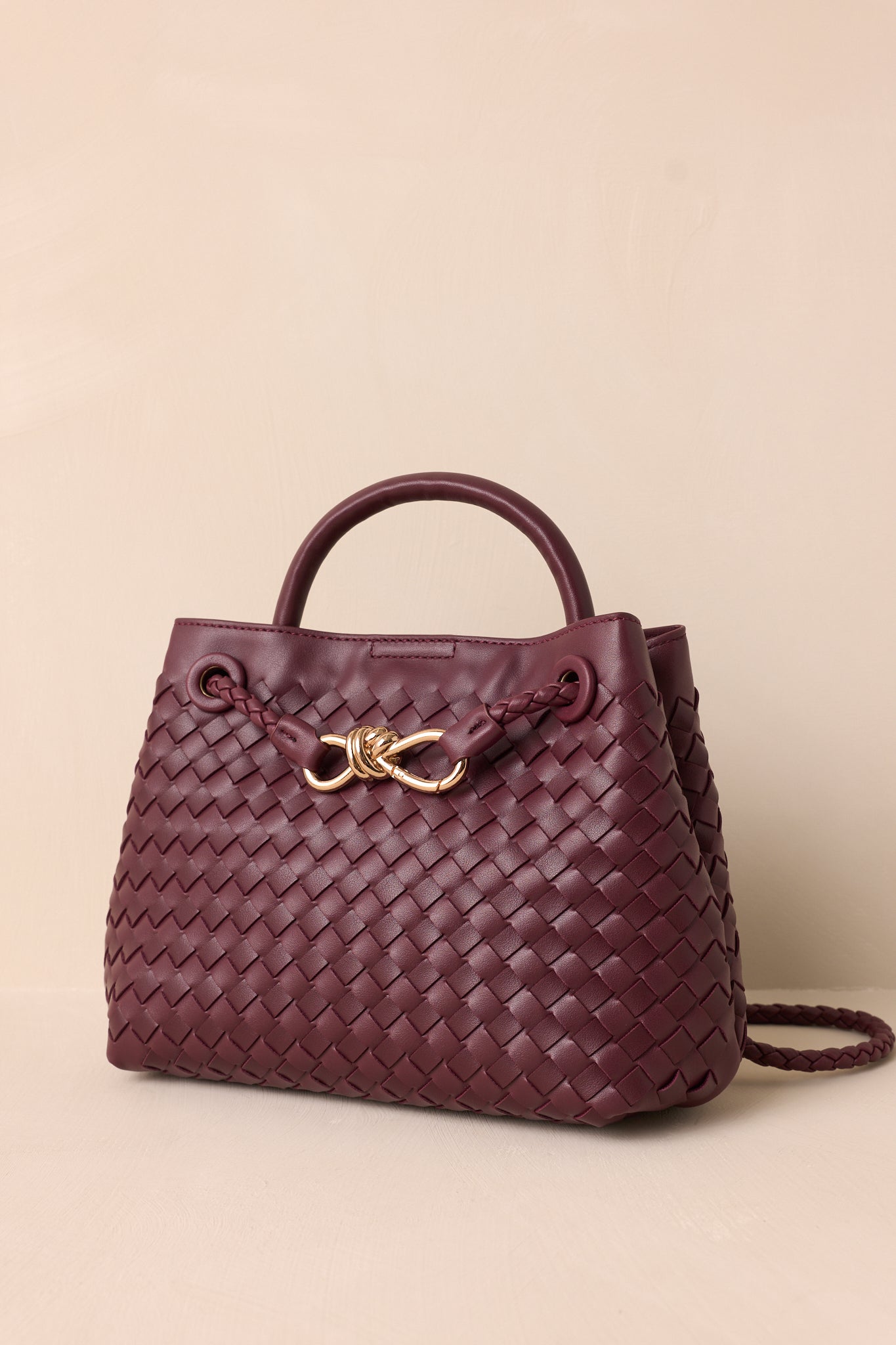 A side view of the wine faux leather bag, highlighting the short handle for handheld use and the long removable woven strap for shoulder use.