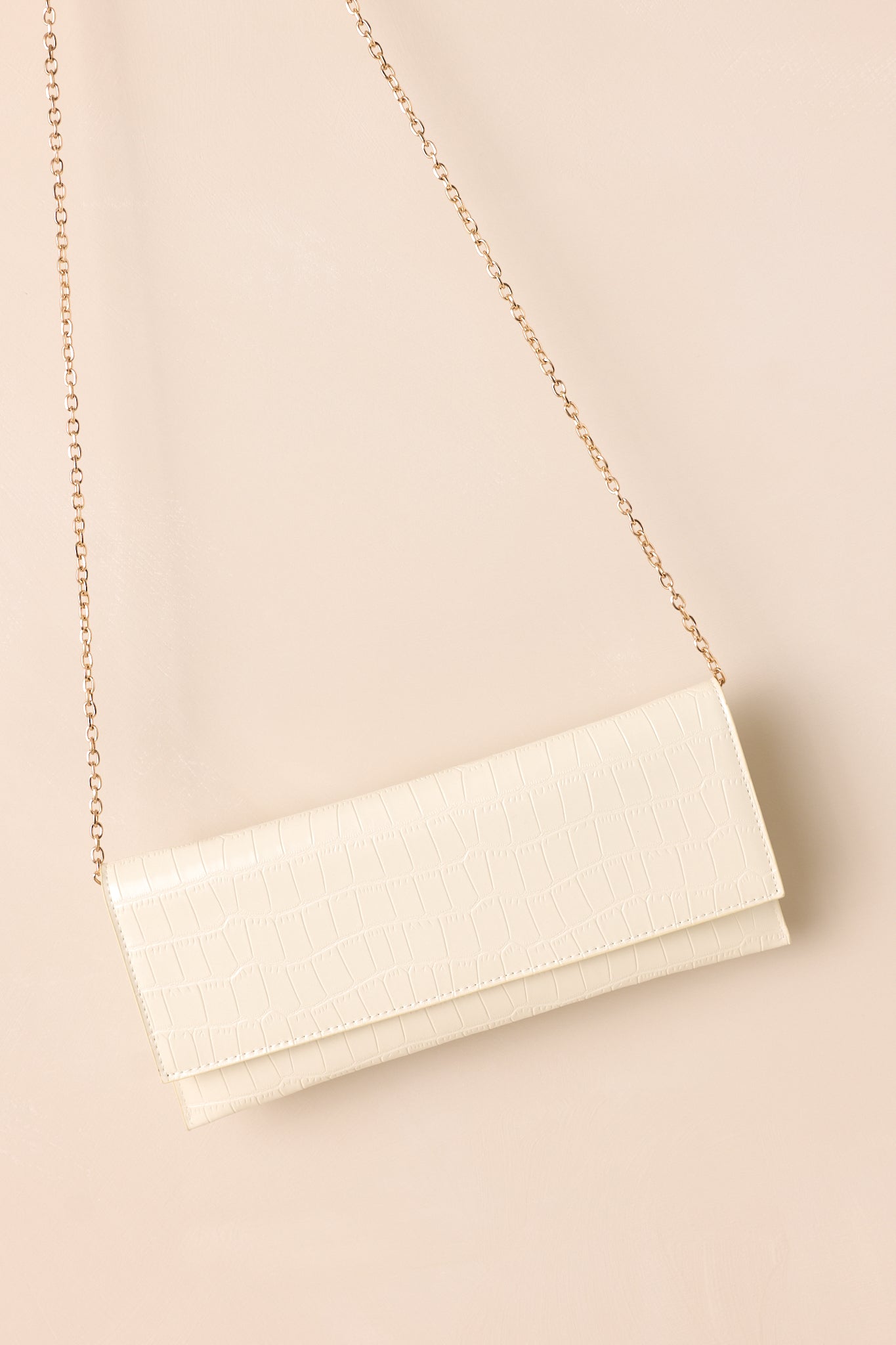 The ivory clutch laid flat on a beige surface, with the optional gold chain strap displayed alongside the bag to emphasize its versatility.