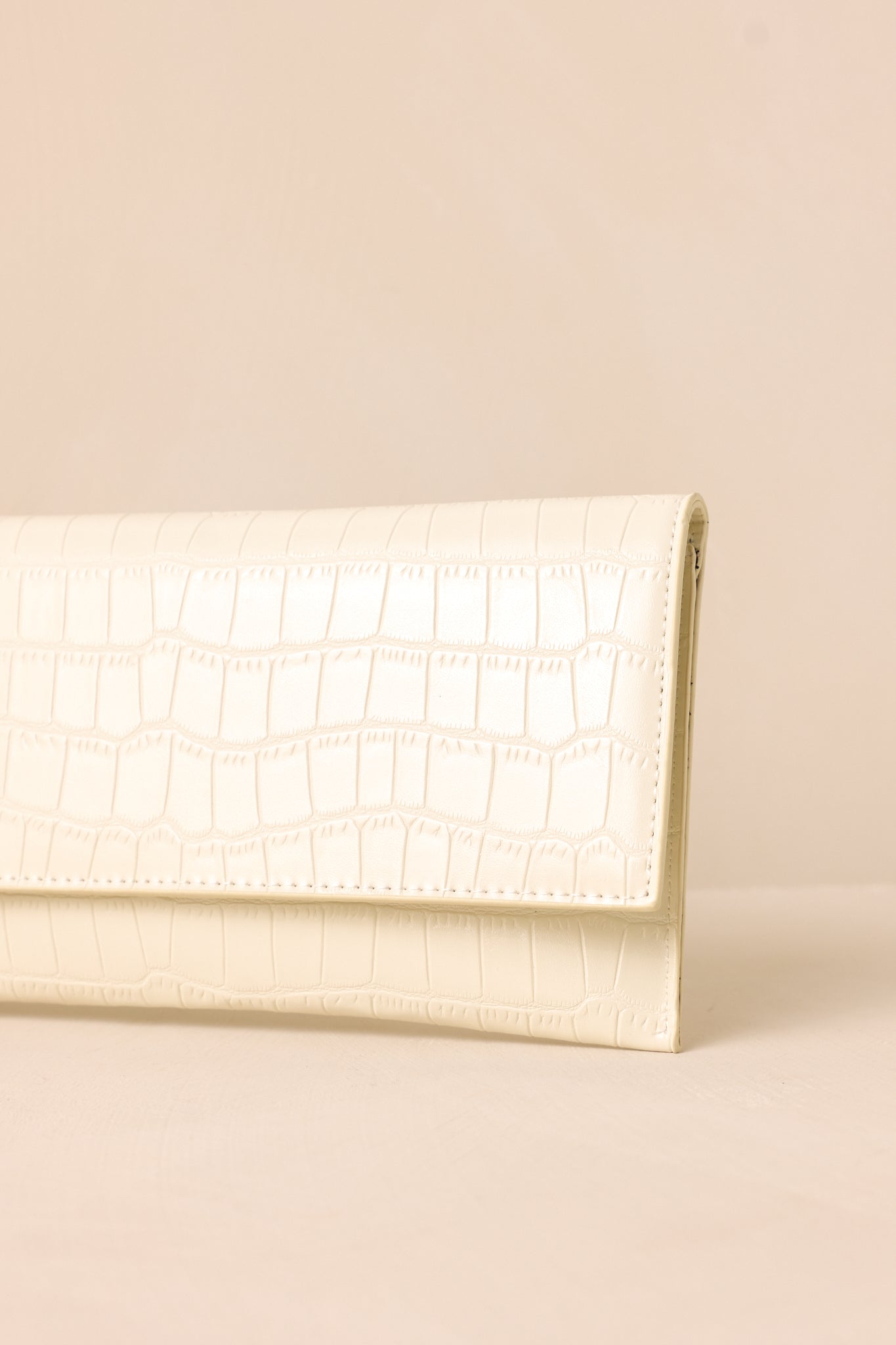 A close-up detail shot of the ivory clutch’s refined stitching of the faux crocodile material.