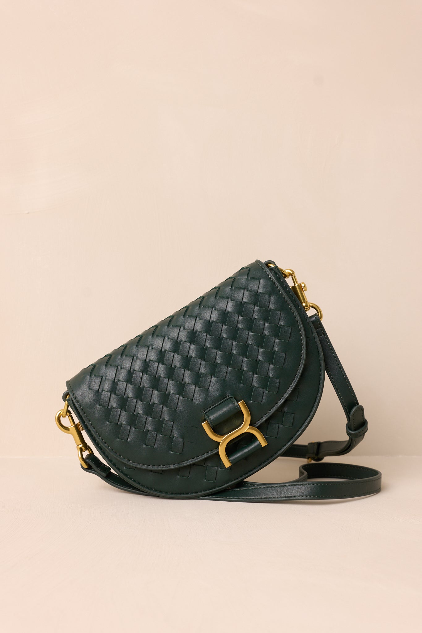 A side angle of the green handbag on a beige background, highlighting the solid green belt-style shoulder strap and the structured silhouette of the design.