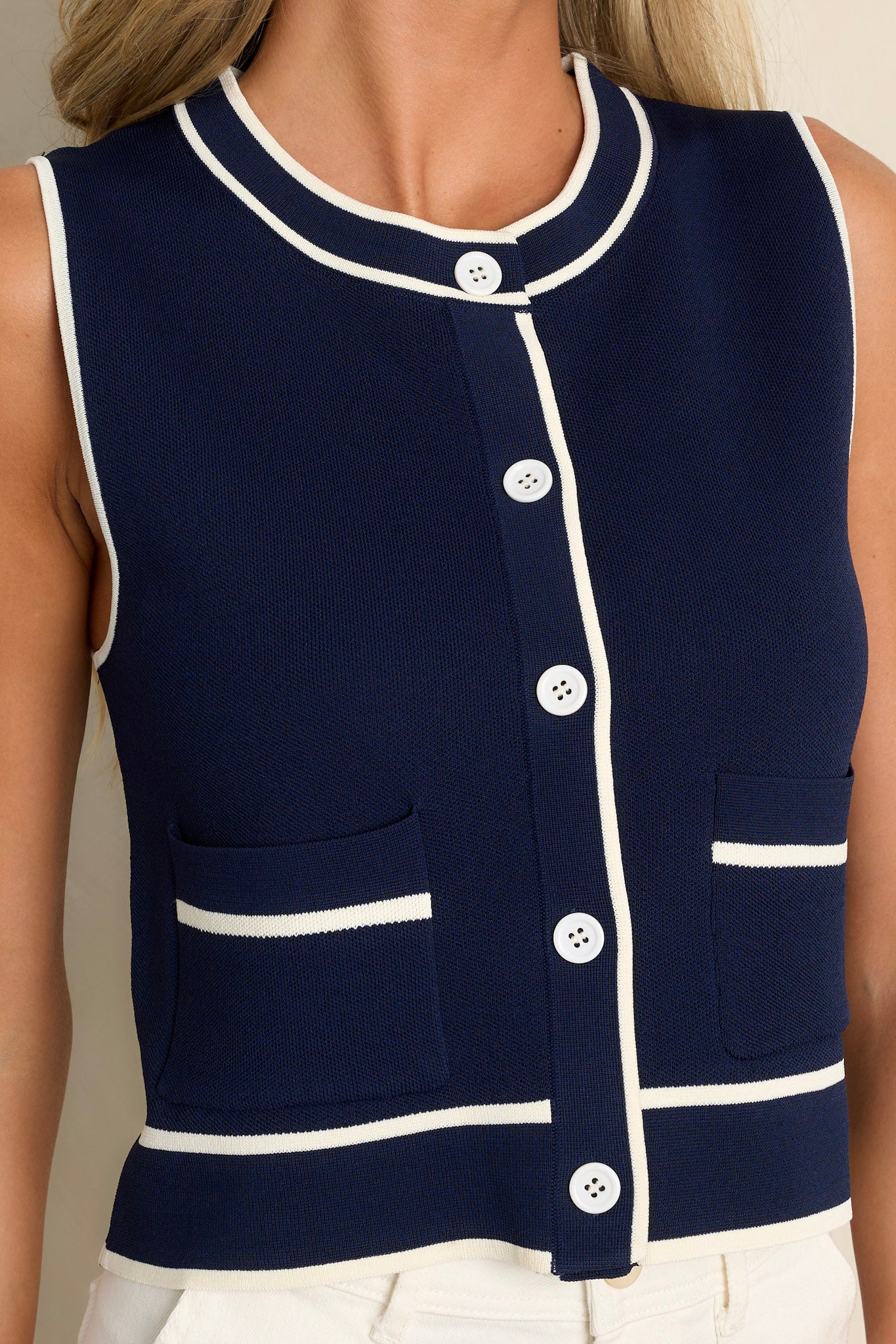 Close-up of the navy vest showing the crew neckline, functional button front, functional pockets, and high contrasting trim.