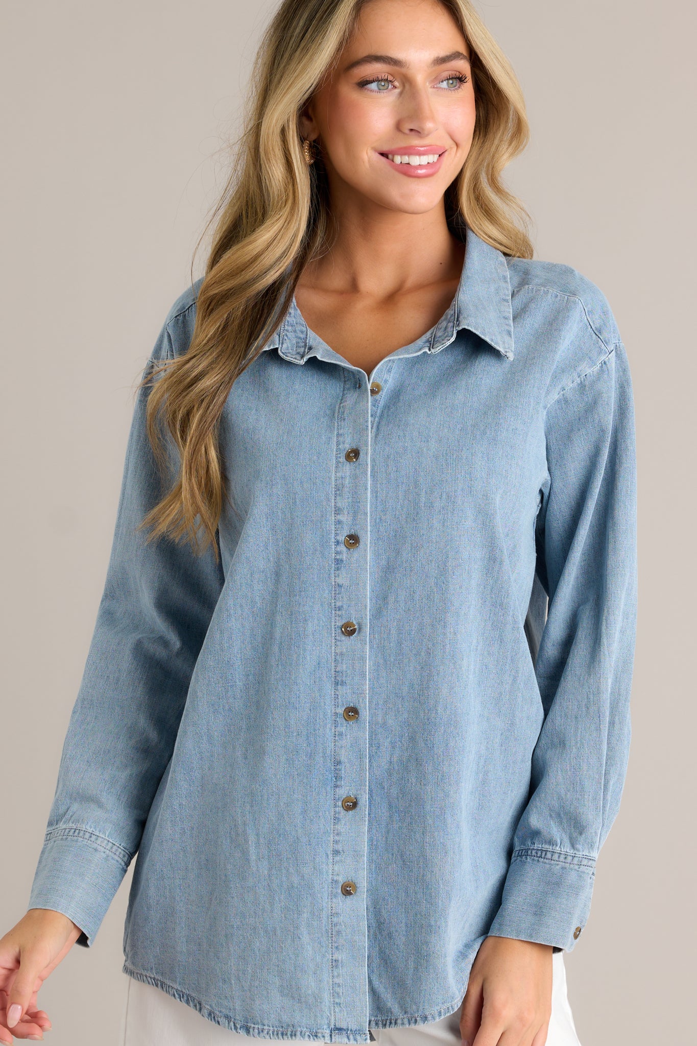 Front angled view of a chambray top featuring a collared neckline, functional buttons down the front, long sleeves with buttoned cuffs, and a scoop bottom hemline