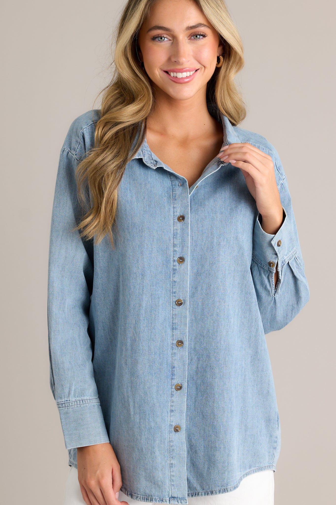 This chambray top features a collared neckline, functional buttons down the front, long sleeves with buttoned cuffs, and a scoop bottom hemline