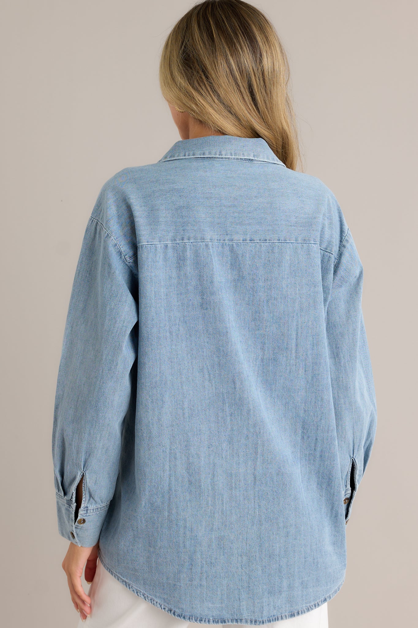 Back view of a chambray top highlighting the overall fit, long sleeves, and scoop bottom hemline.