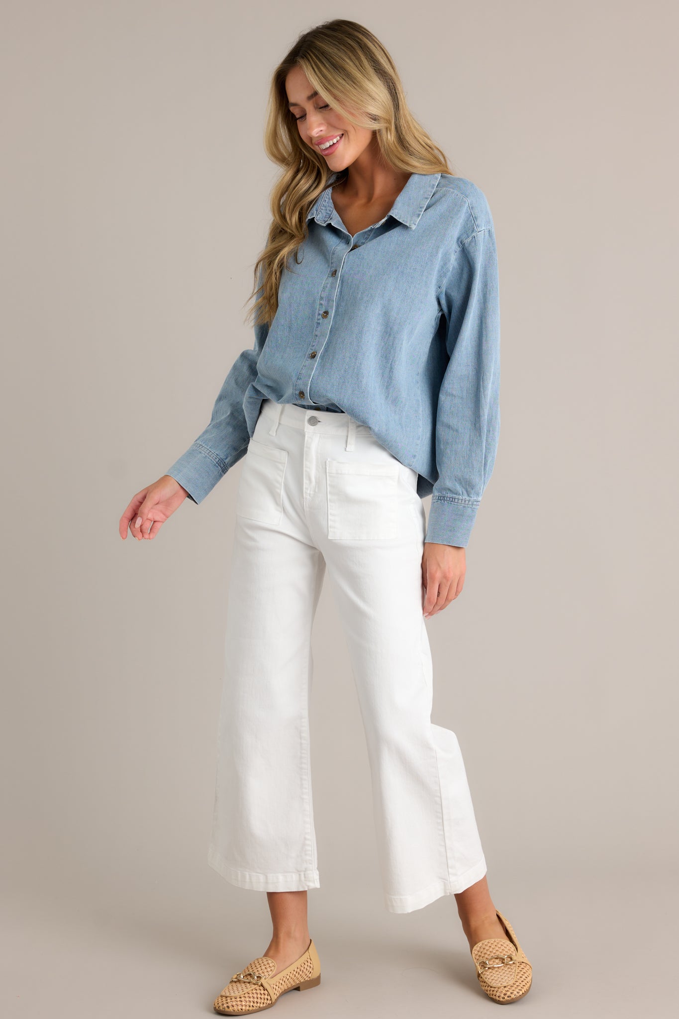 Action shot of a chambray top displaying the fit and movement, highlighting the collared neckline, functional buttons, long sleeves with buttoned cuffs, and scoop bottom hemline.