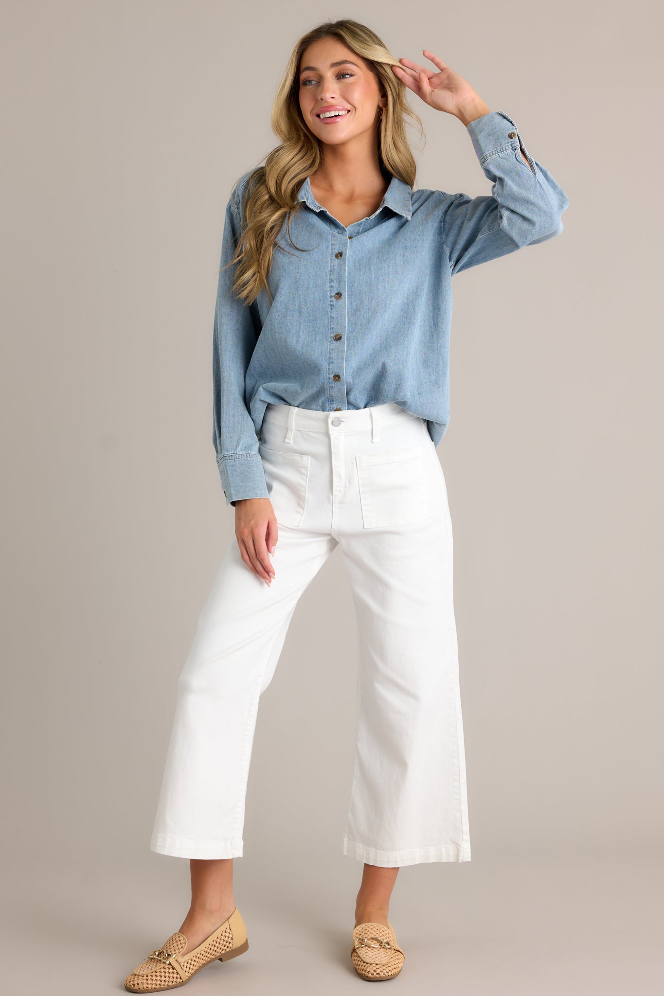 Front view of a chambray top featuring a collared neckline, functional buttons down the front, long sleeves with buttoned cuffs, and a scoop bottom hemline.