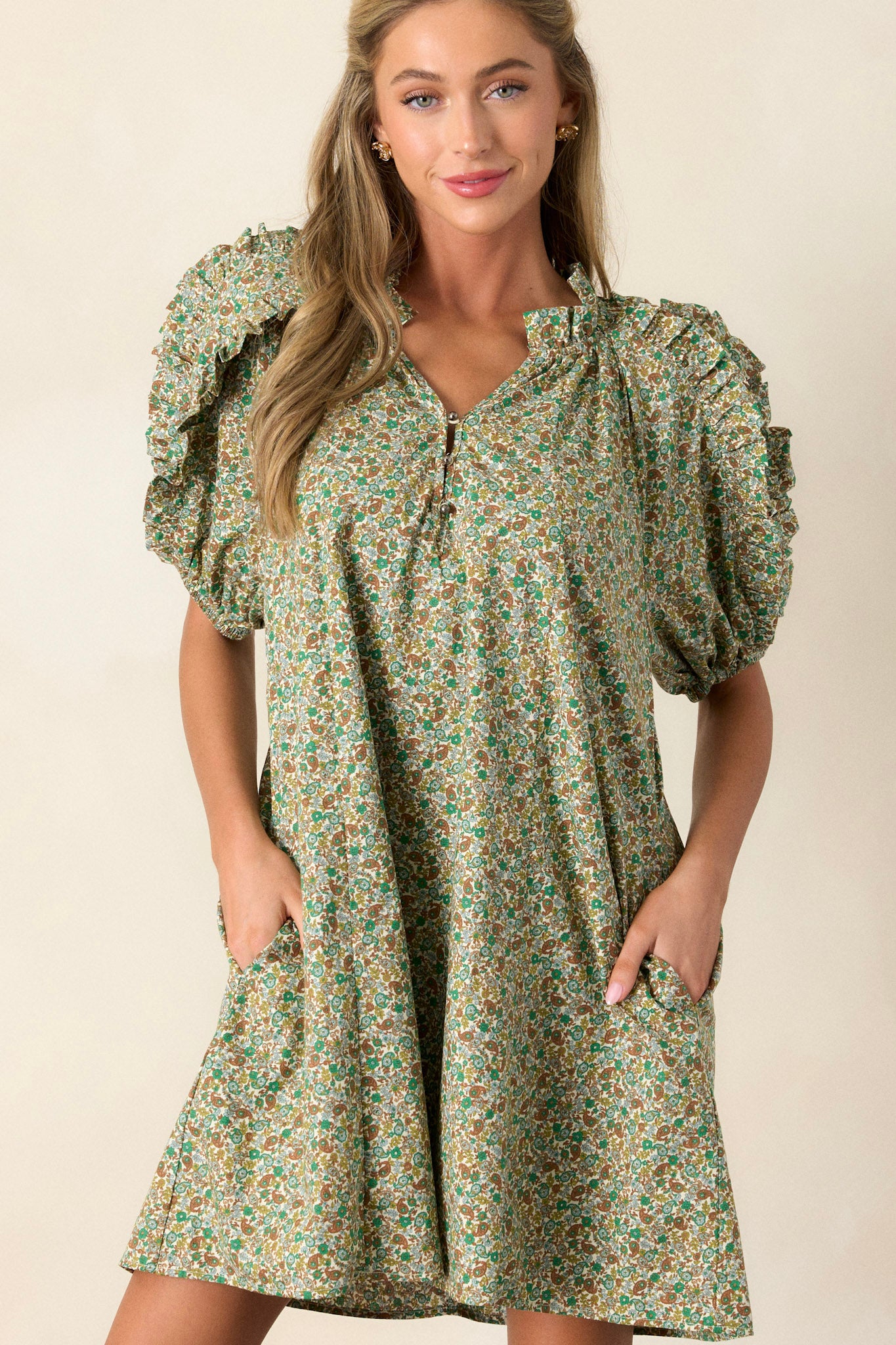 Front view of a playful and unique green dress featuring flouncy bubble sleeves, a small v-neck, fun frills, and two functional side pockets.