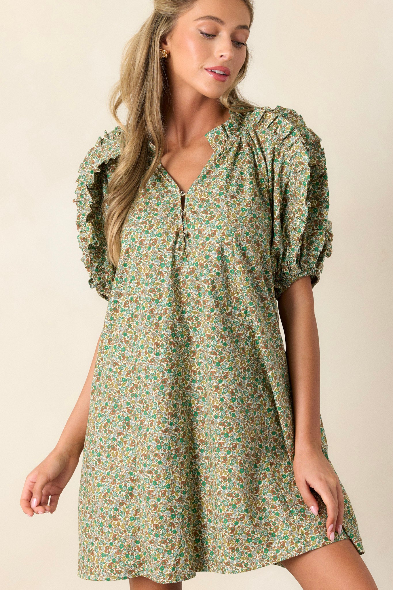 Front angled view of a playful and unique green dress featuring flouncy bubble sleeves, a small v-neck, fun frills, and two functional side pockets