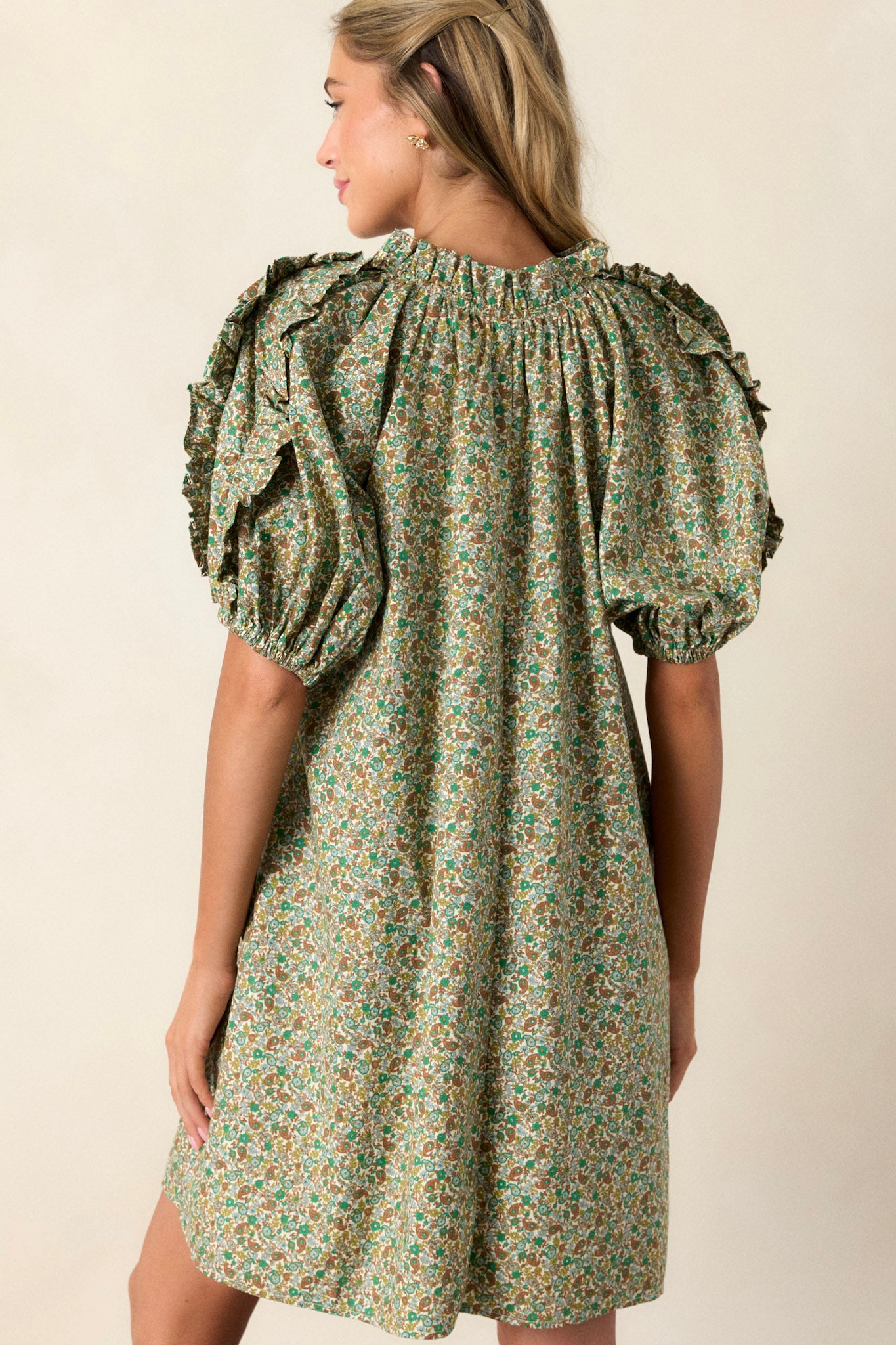 Back view of a playful and unique green dress highlighting the flouncy bubble sleeves and the frills.