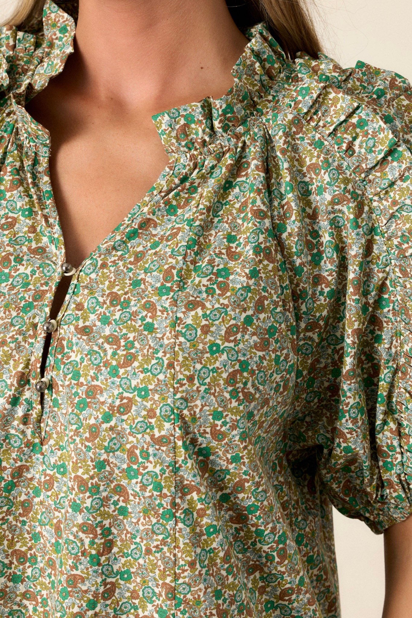  Close-up of a playful and unique green dress showing the small v-neck, flouncy bubble sleeves, and the texture of the fun frills.