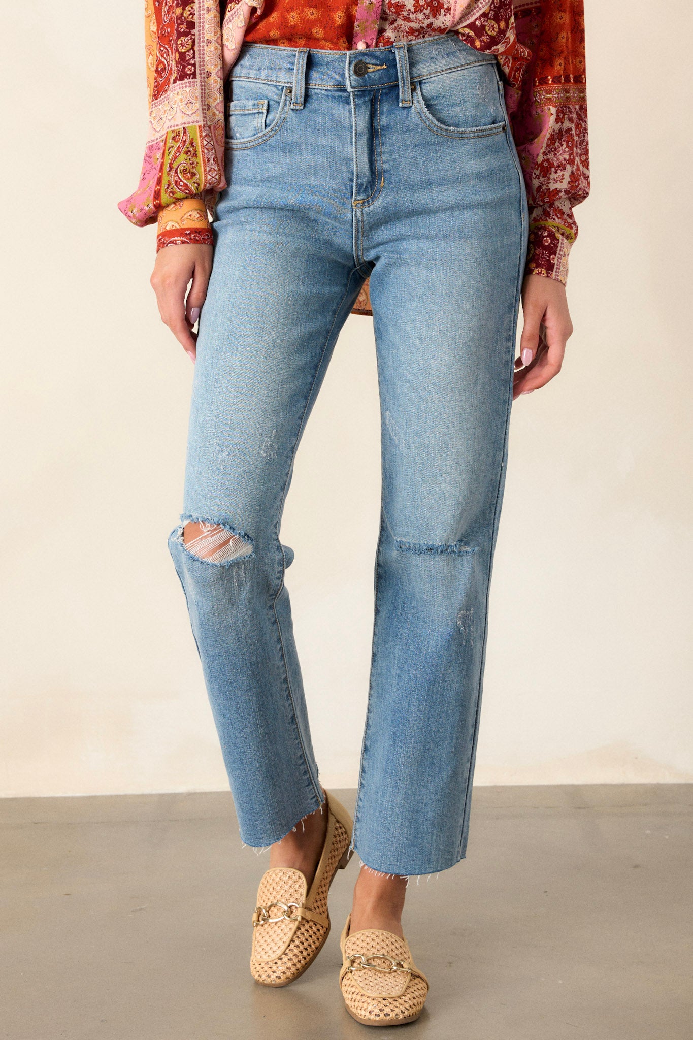 Front angled view of jeans featuring a high waisted design, button and zipper closure, belt loops, functional front and back pockets, distressing, and a raw hemline